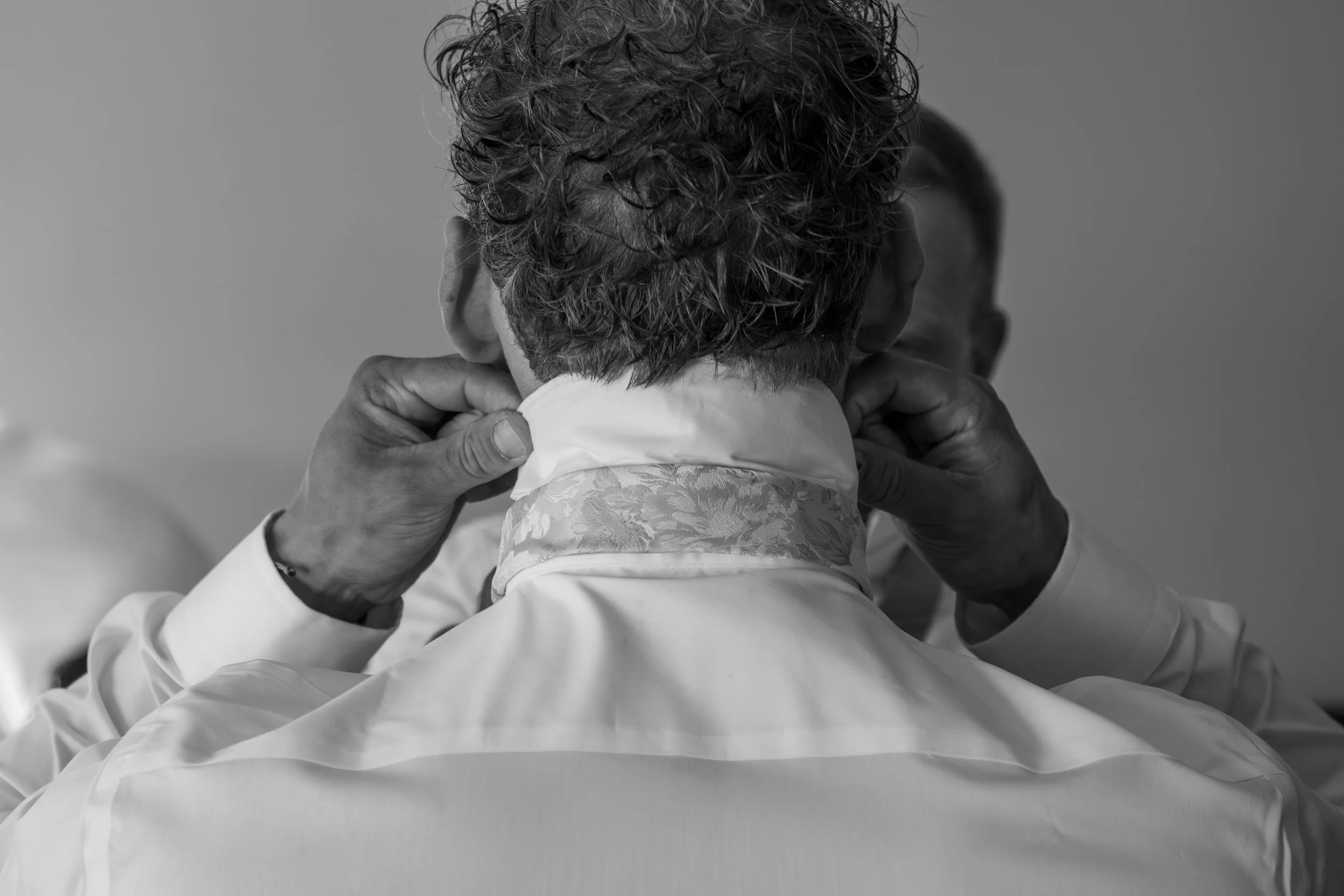 A woman with curly hair is being helped with her collar by another person, in black and white.