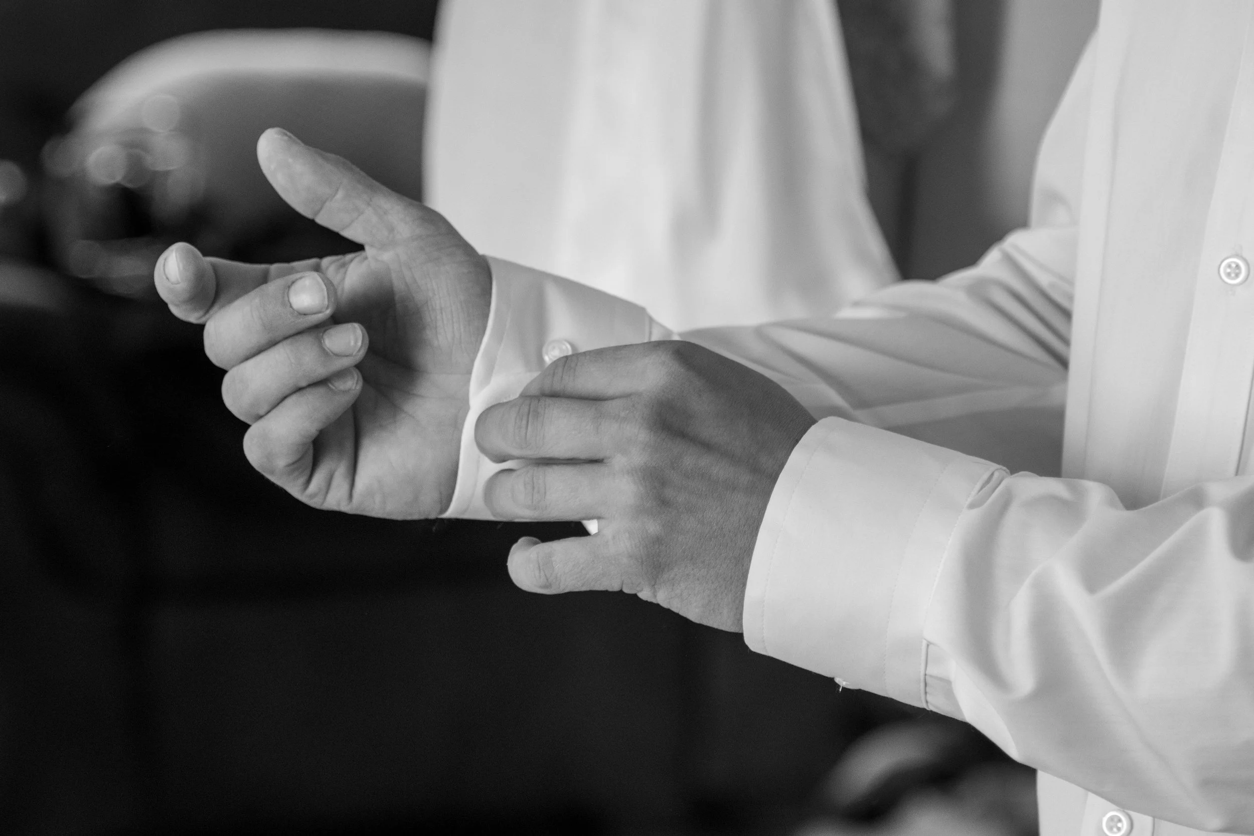 Close-up of a person's hands, with one finger pointing, wearing a white long-sleeve shirt, in black and white.