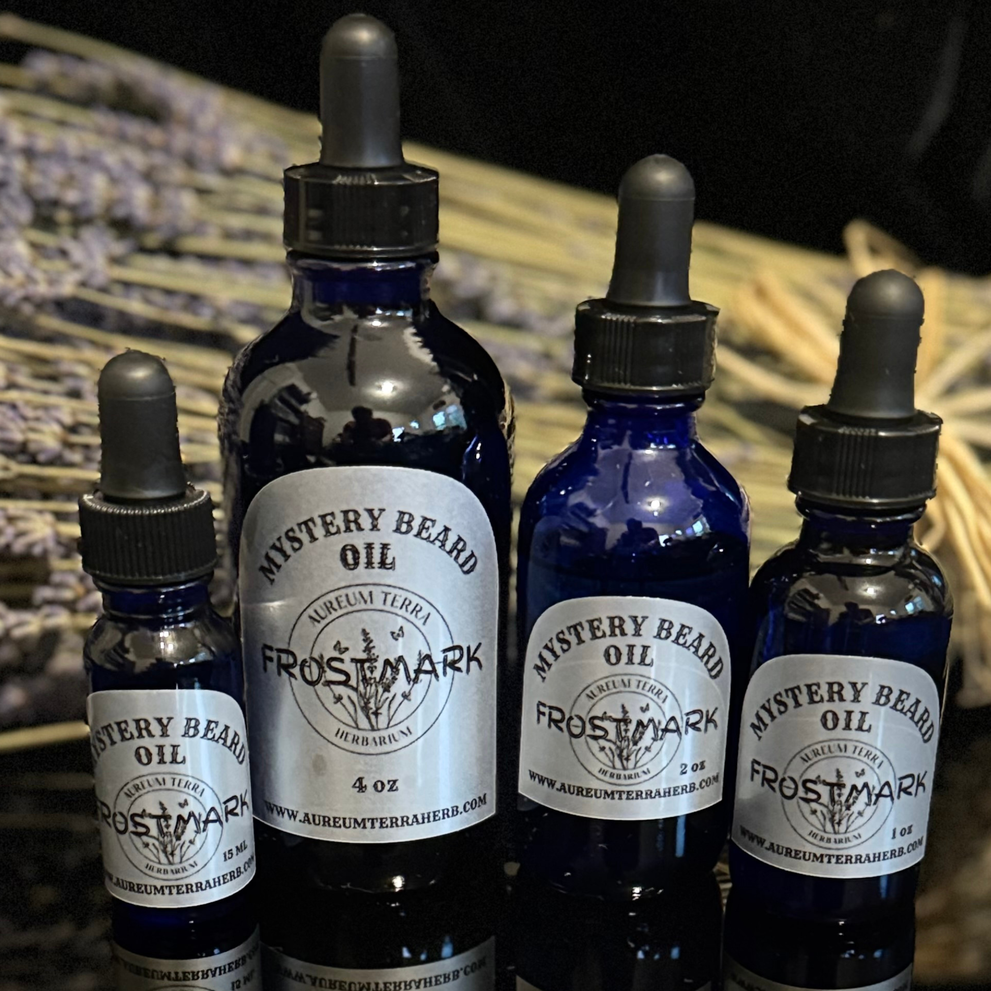 Four cobalt-blue glass dropper bottles labeled Mystery Beard Oil – Frostmark by Aureum Terra Herb's displayed against a background of dried lavender. Represents Frostmark beard oil collection featuring handcrafted, aromatic, and conditioning blends m