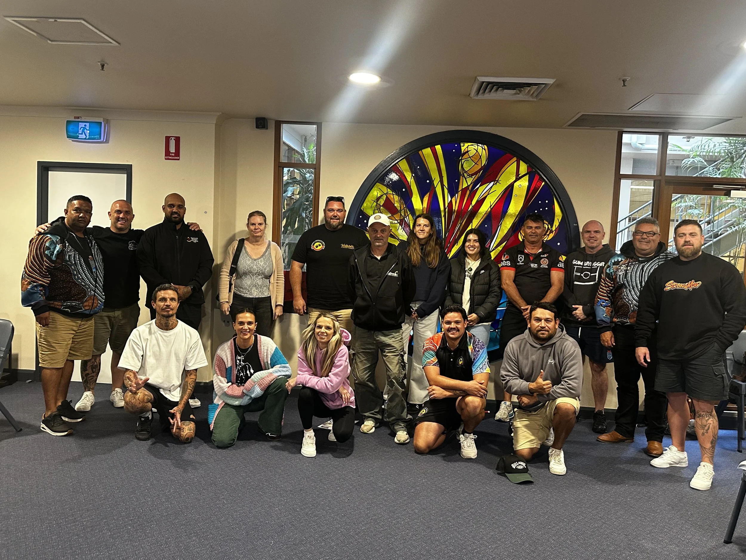 Group of people posing for a photo indoors with colorful art in the background.