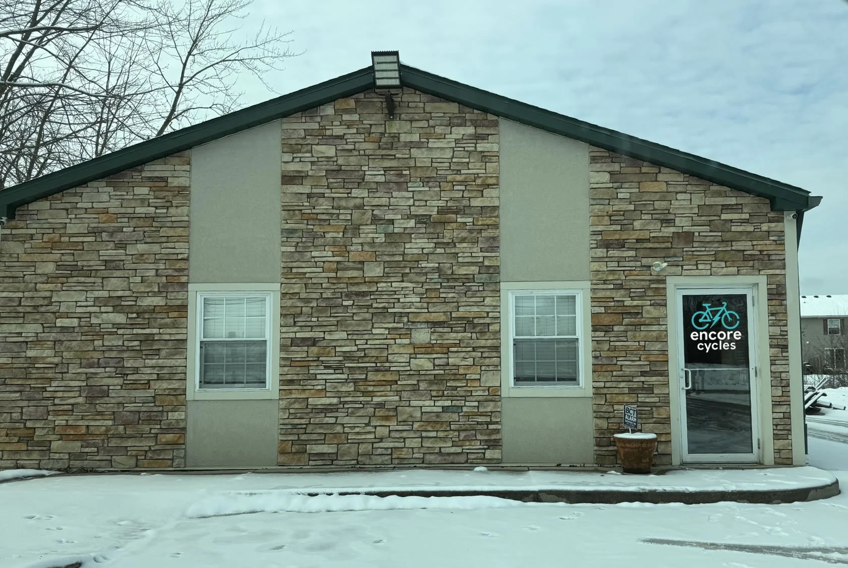 A brick building with a sign that reads 'Encore Cycles' and a blue bicycle icon on the door, in a snowy landscape.