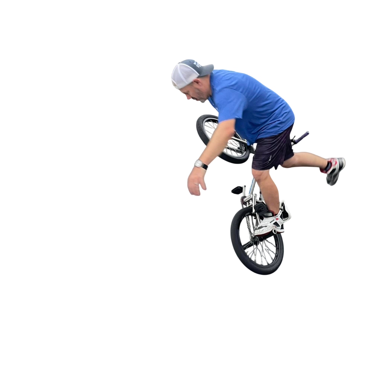 Man performing a BMX stunt, balancing on his front wheel with one leg extended backward and the other on the pedal, wearing a blue shirt, black shorts, a gray cap, and white sneakers.