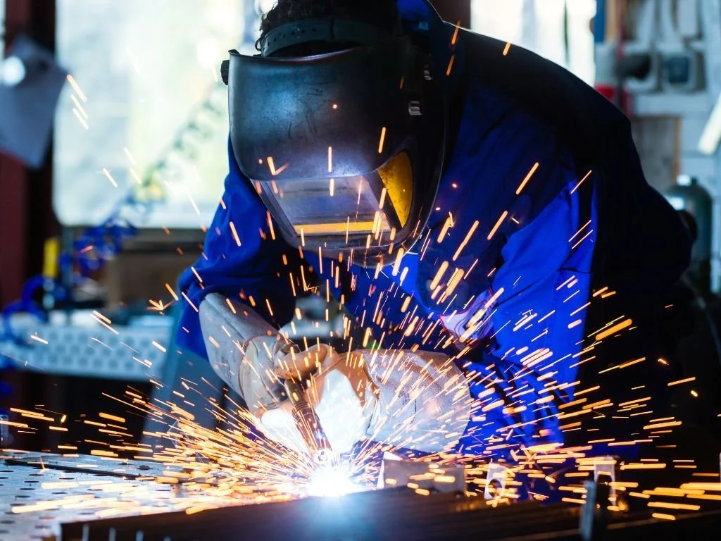 Person welding metal, with sparks flying in workshop.