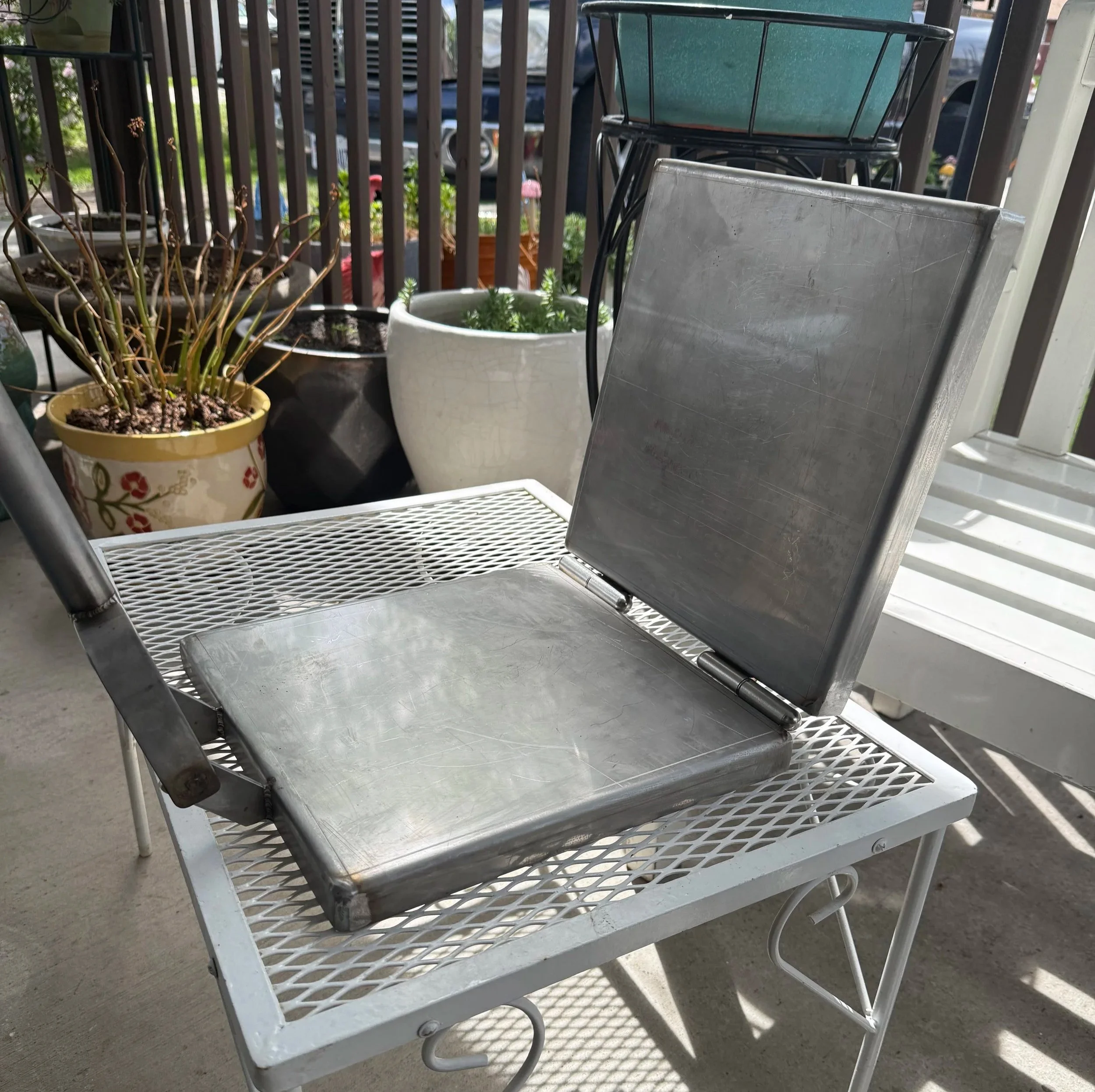 Metal chair on a porch with potted plants and a metal basket on top.