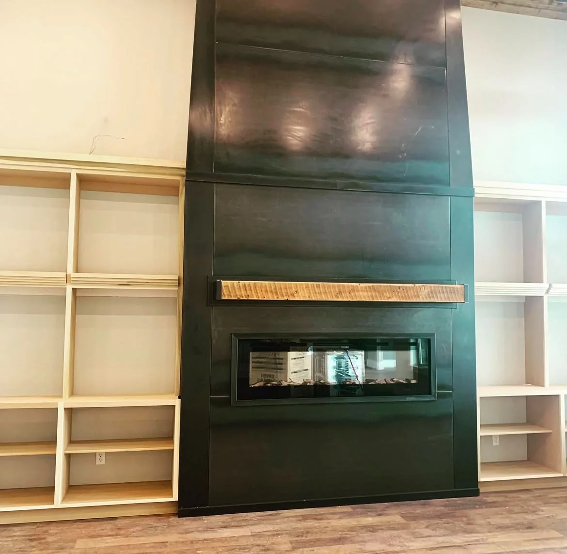 Modern living room with a black fireplace and wood mantel, flanked by two empty beige wooden shelves.