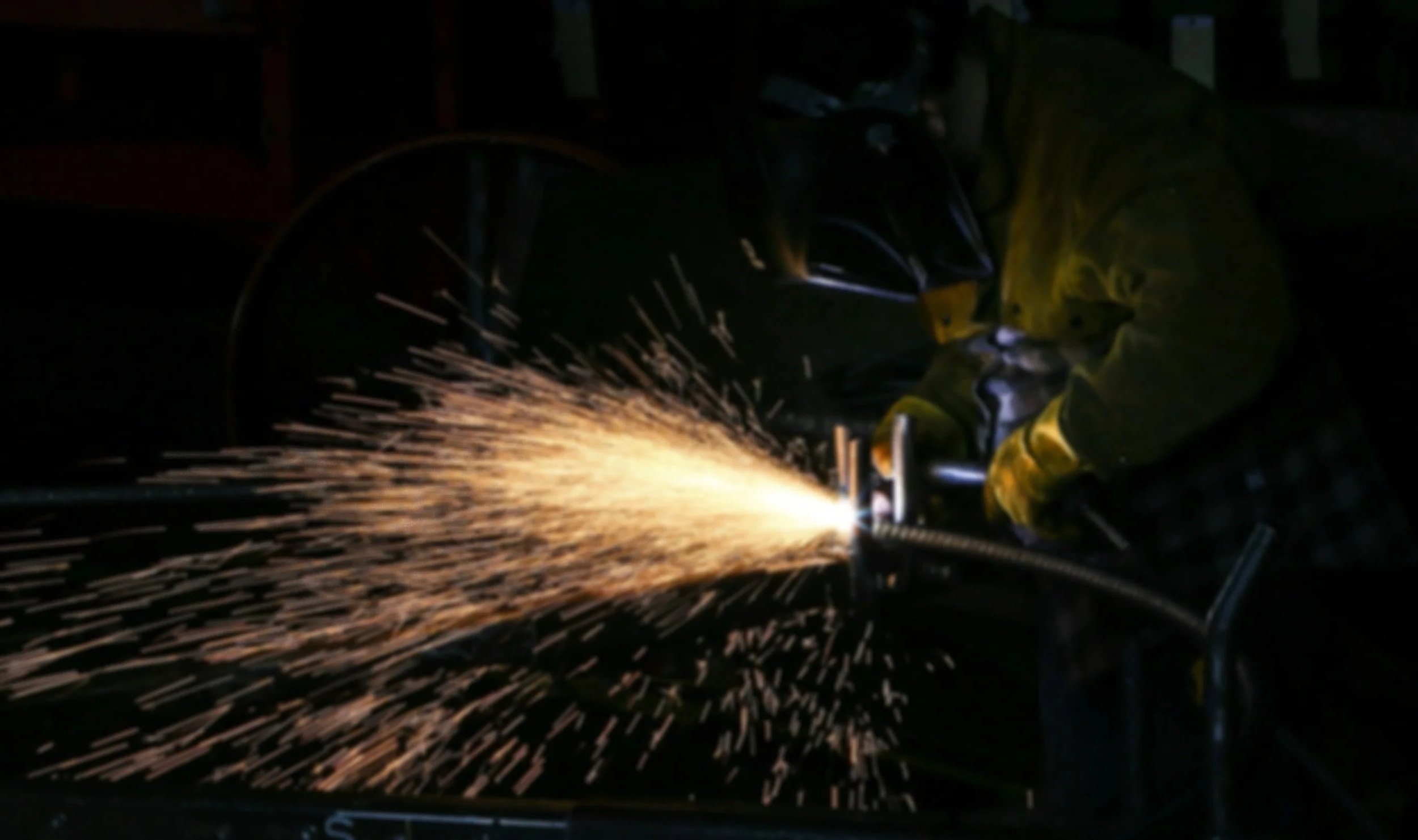 A person welding metal with sparks flying in a dark environment.