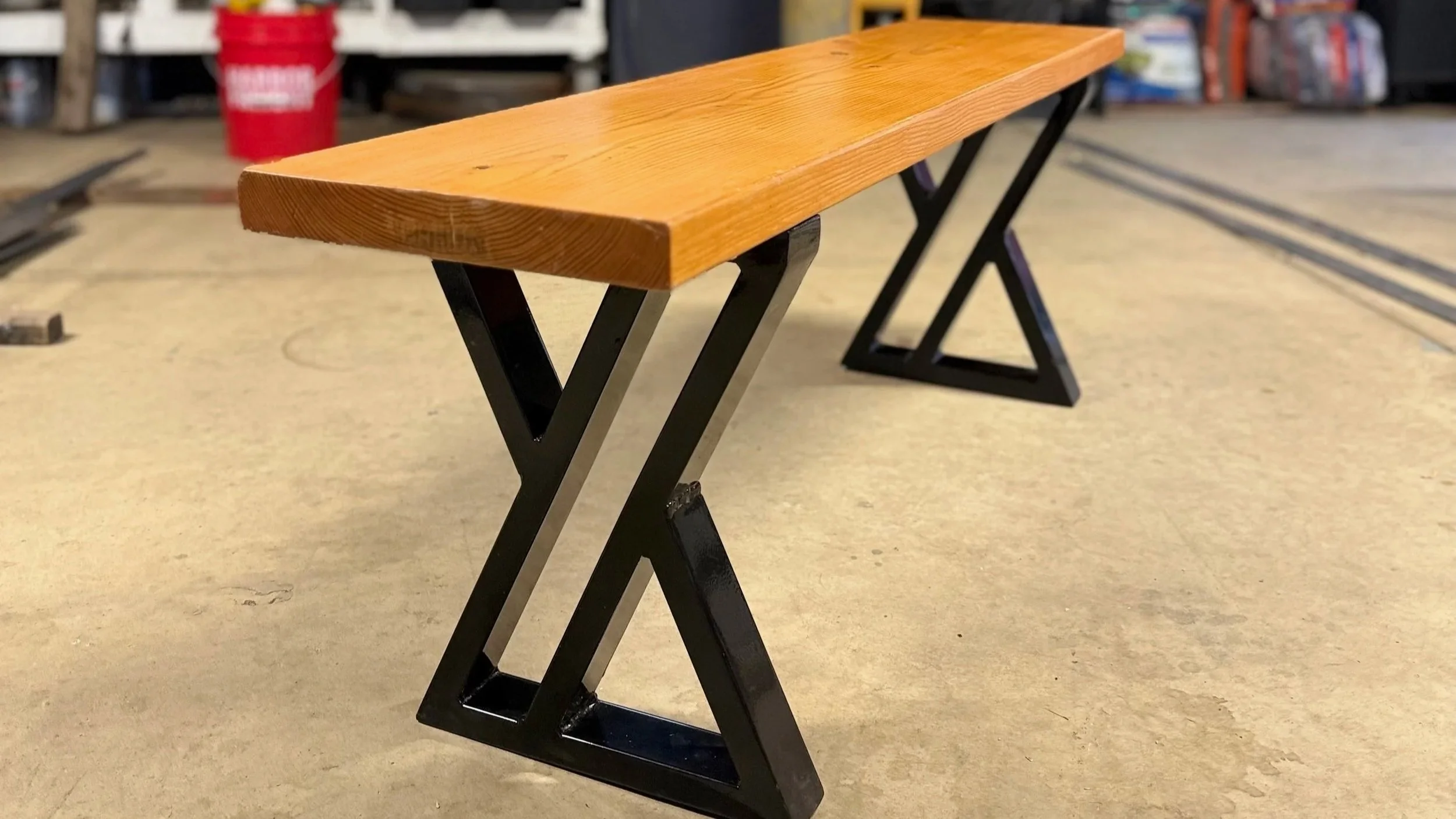 A wooden bench with black metal X-shaped legs in a workshop.