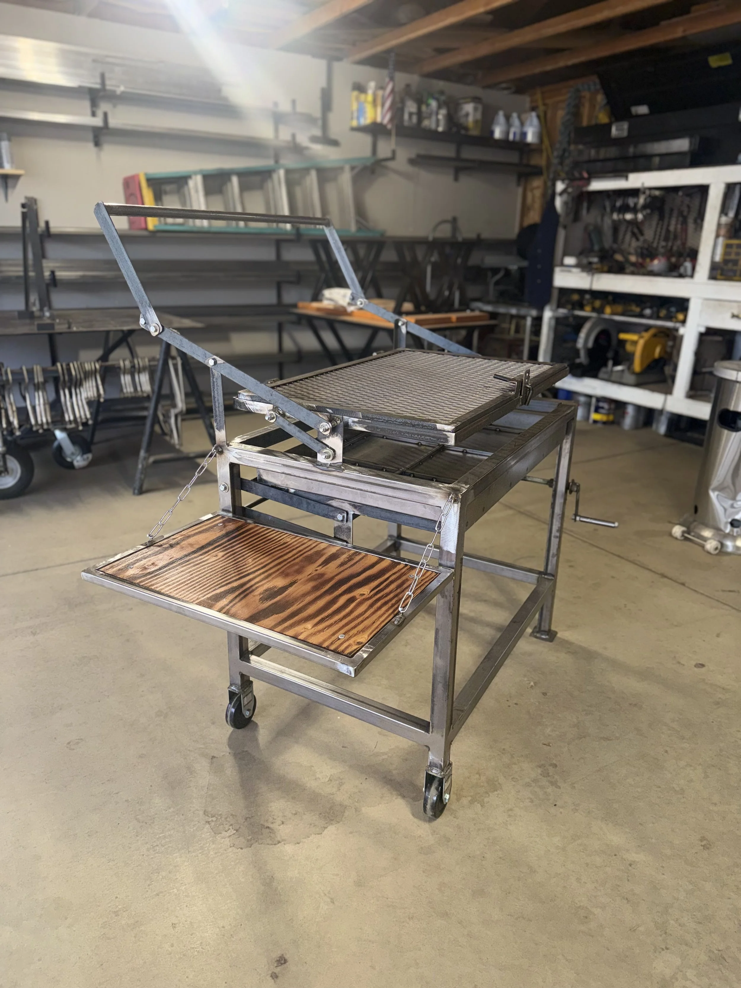A metal cart with wooden shelves in a garage workshop, with various tools and equipment on shelves and workbenches in the background.