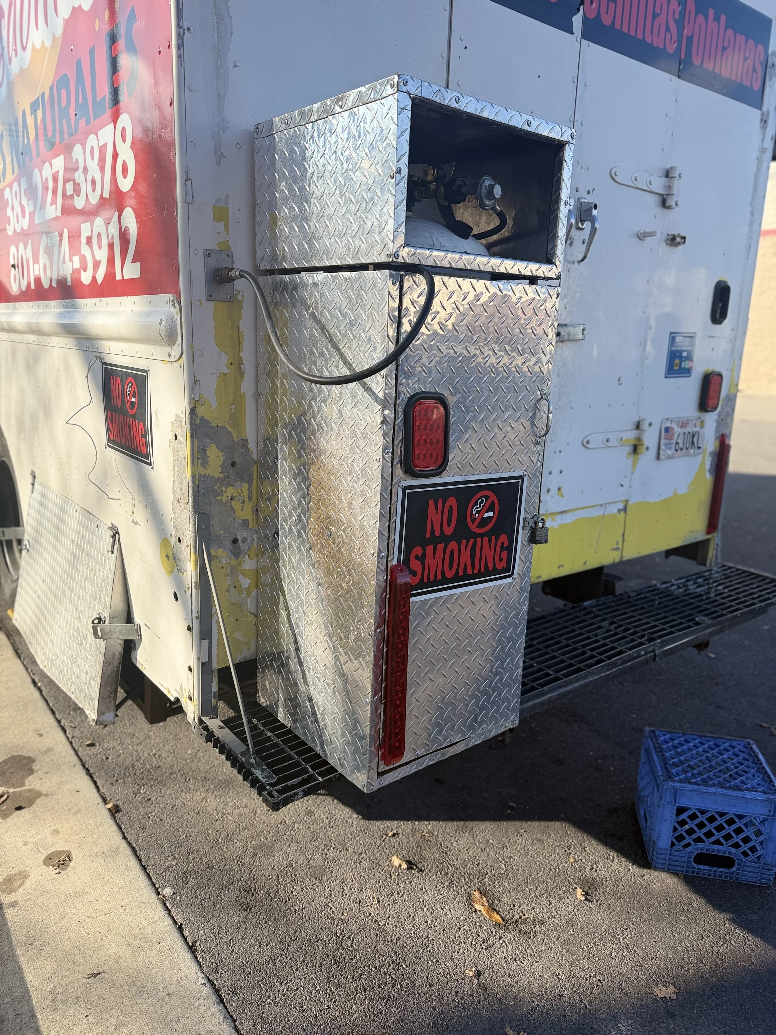 The image shows the back of an emergency or utility vehicle with a diamond plate metal compartment and red warning lights, with a