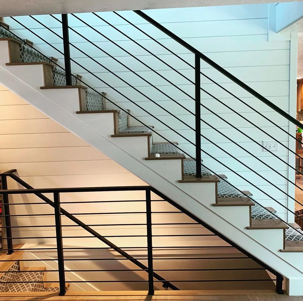 Interior view of a staircase with black metal railings and wooden stairs, carpeted with a black and white patterned rug, in a modern home.