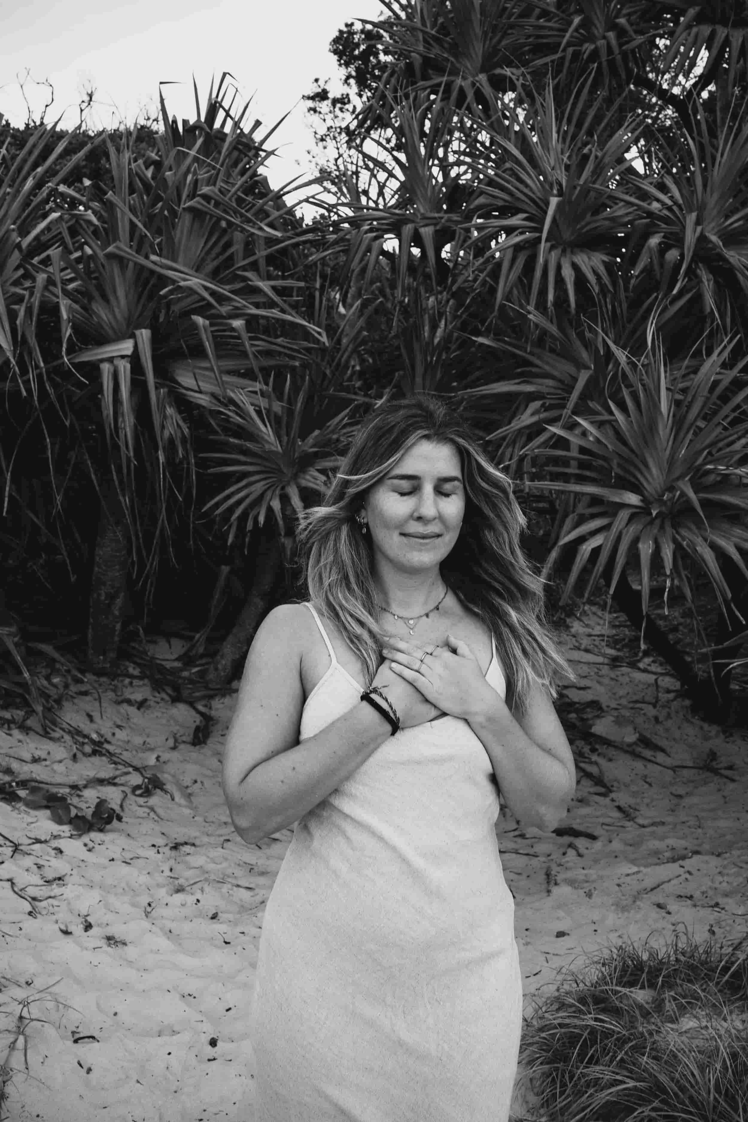 woman surrounded by palm trees in nature holding both hands on her heart