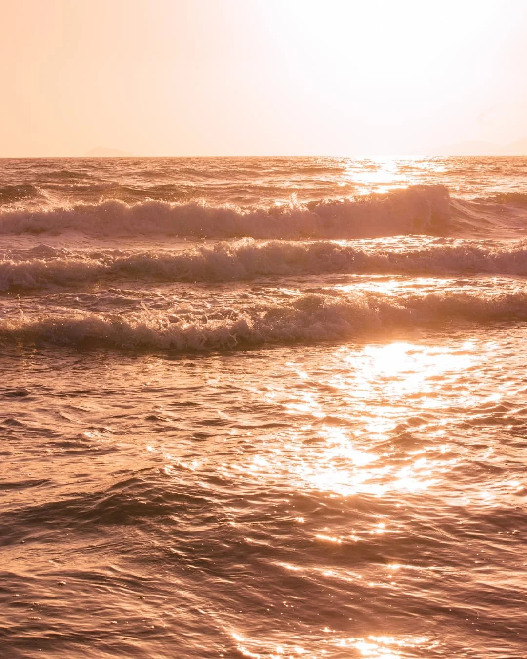 Sunset over the ocean with waves and reflections on the water.