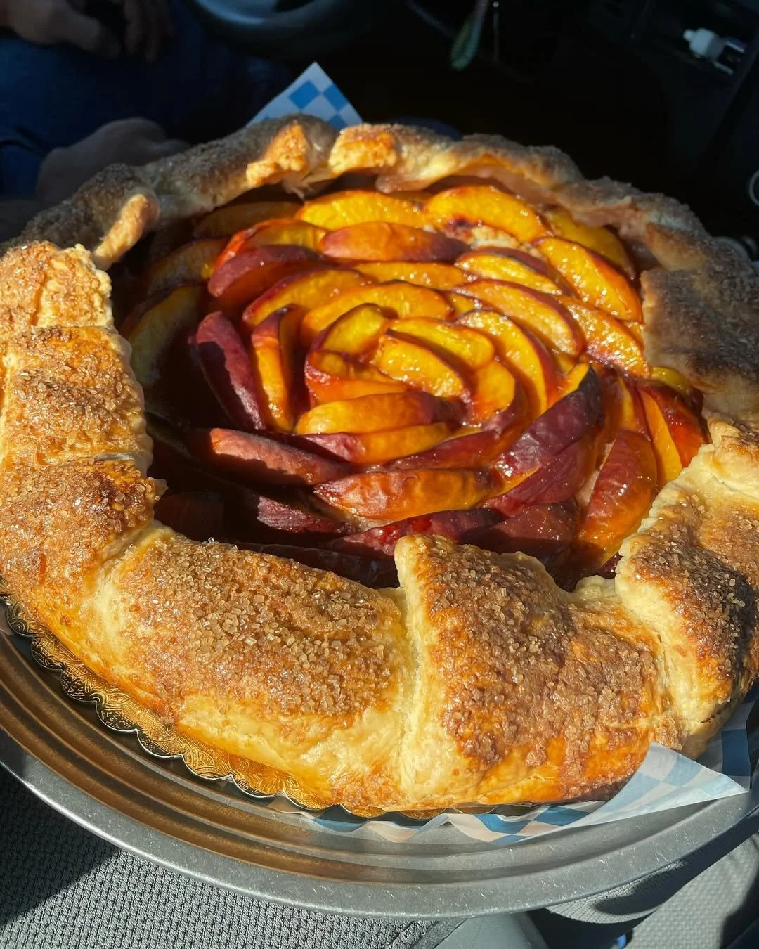 A peach galette with a rustic, flaky crust, filled with sliced peaches, sitting on a silver tray.