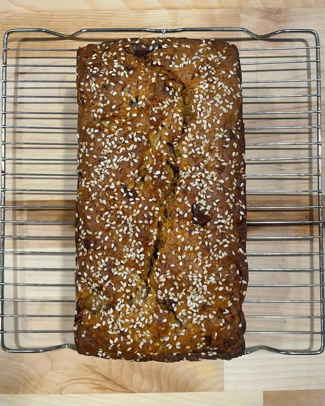 Homemade banana bread topped with sesame seeds cooling on a wire rack.