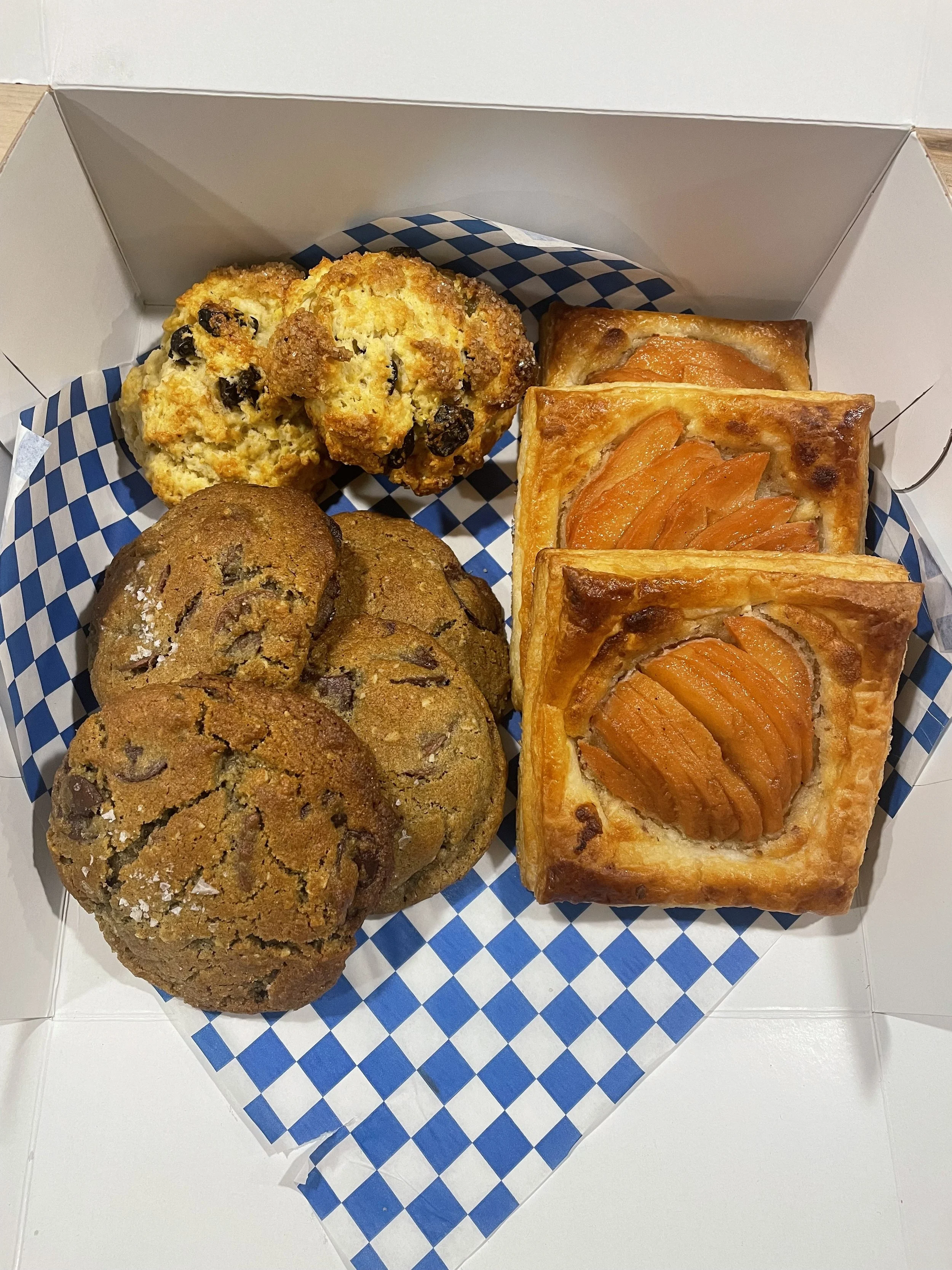 Box of assorted baked goods including chocolate chip cookies, oatmeal raisin cookies, and peach Danish pastries.