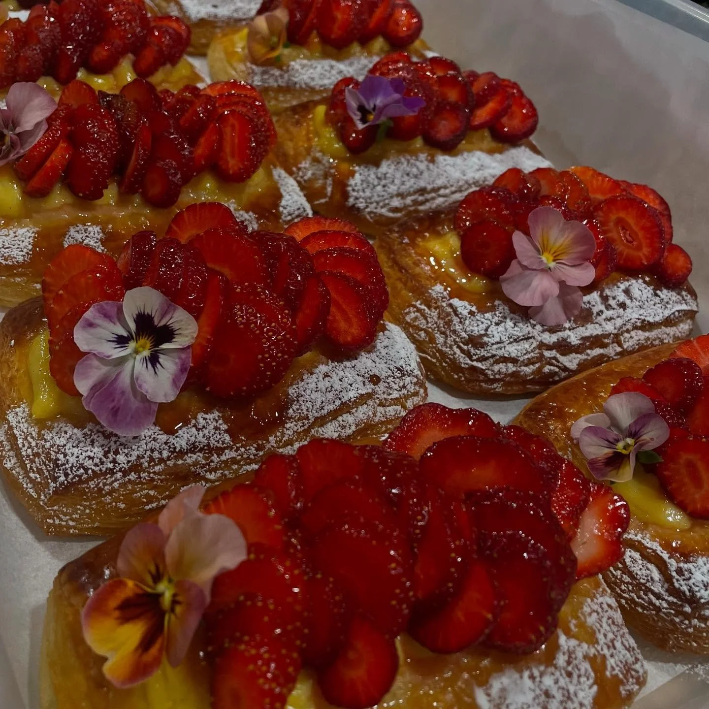 Pastries topped with sliced strawberries, edible flowers, and powdered sugar.
