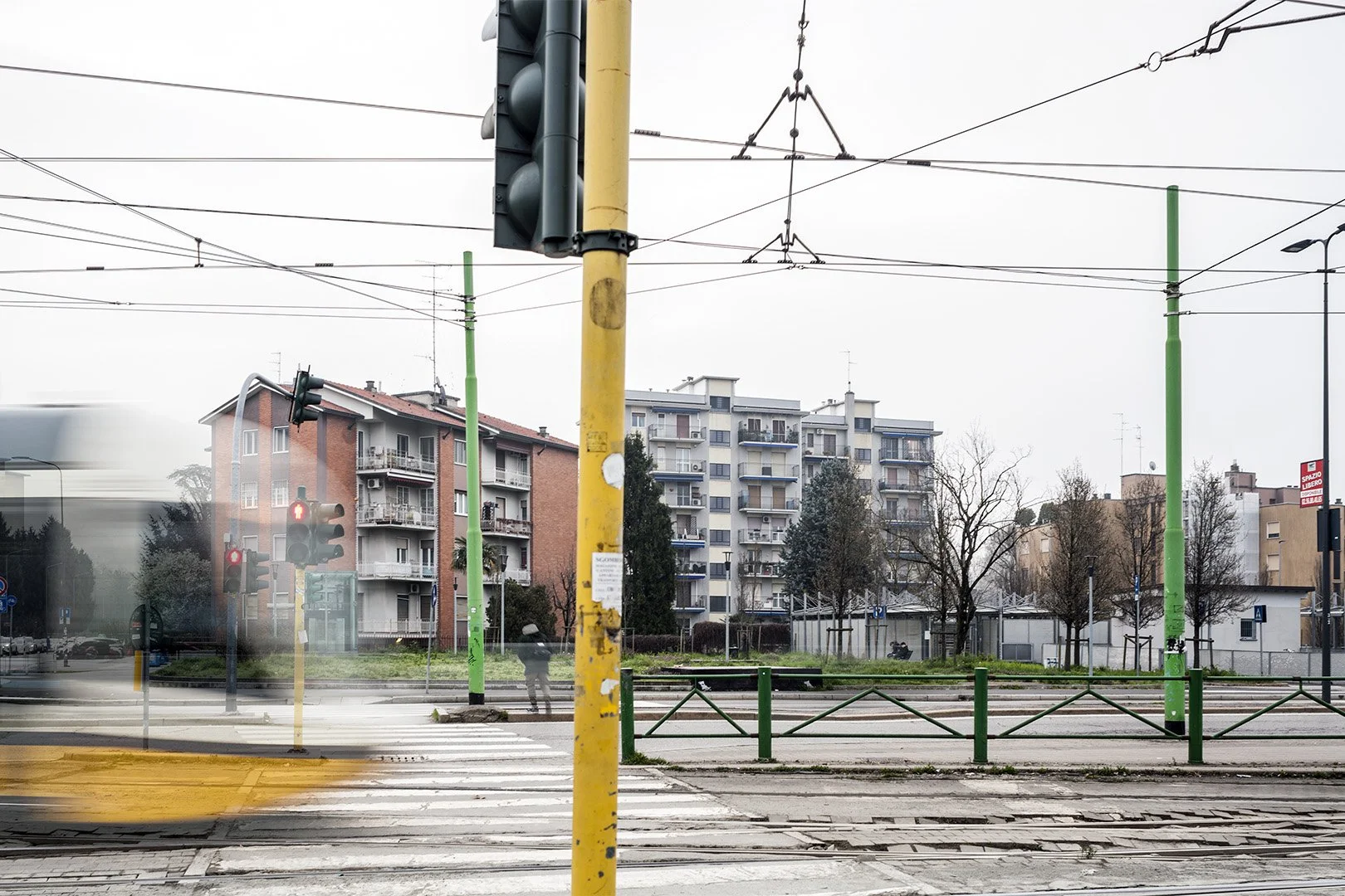 Tram e semafori rossi a un incrocio in un'area urbana con edifici residenziali e alberi, su un cielo nuvoloso.