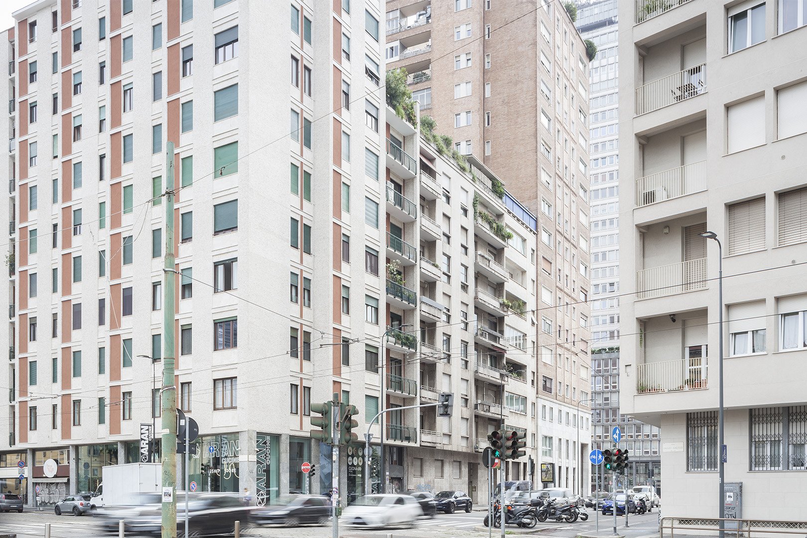 Edifici alti con negozi al piano terra, traffico e veicoli in una strada urbana.