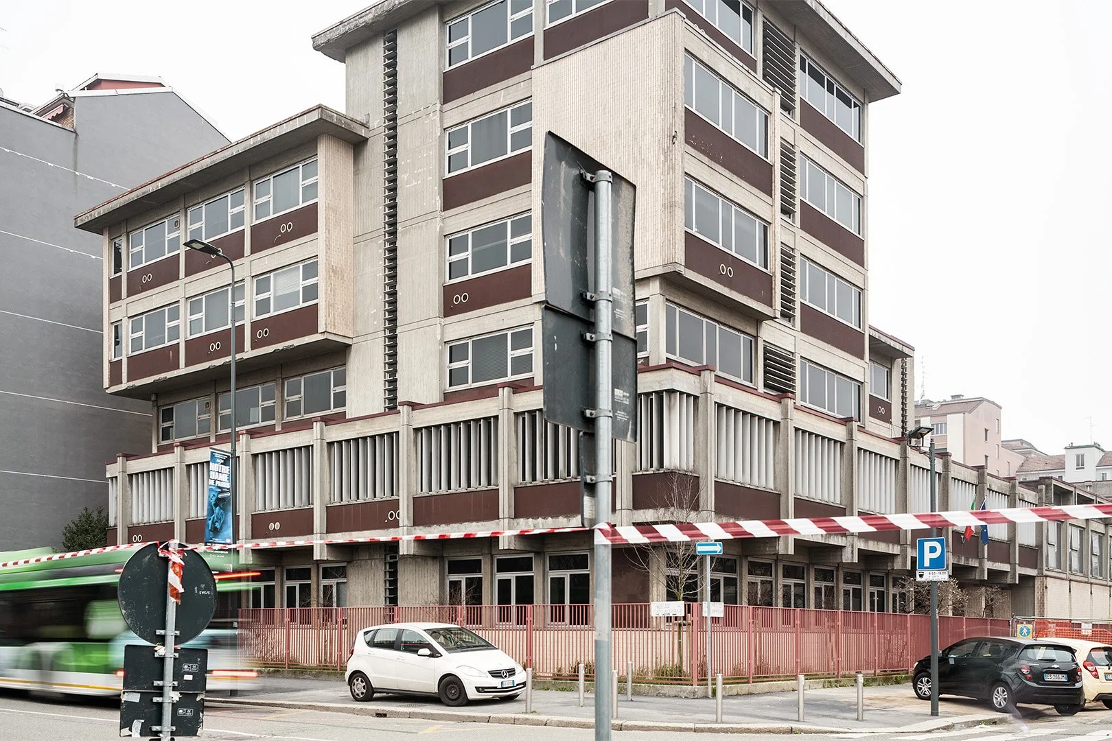 Edificio moderno con balconi e grandi finestre, in un'area urbana, con auto parcheggiate e una strada trafficata.