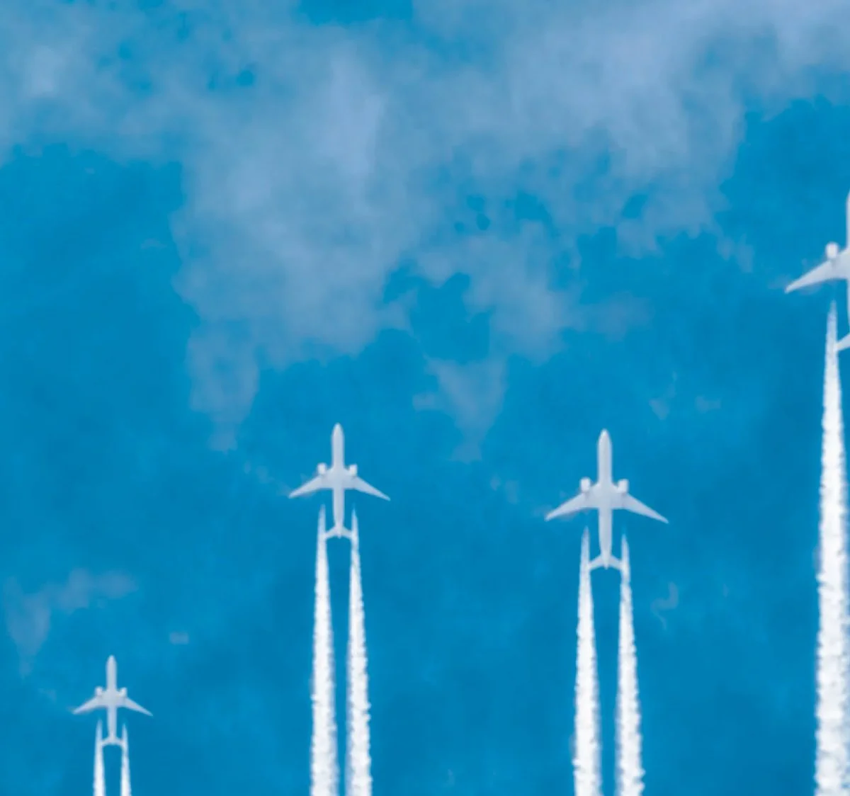 Four fighter jets flying in formation with contrails against blue sky with scattered clouds.