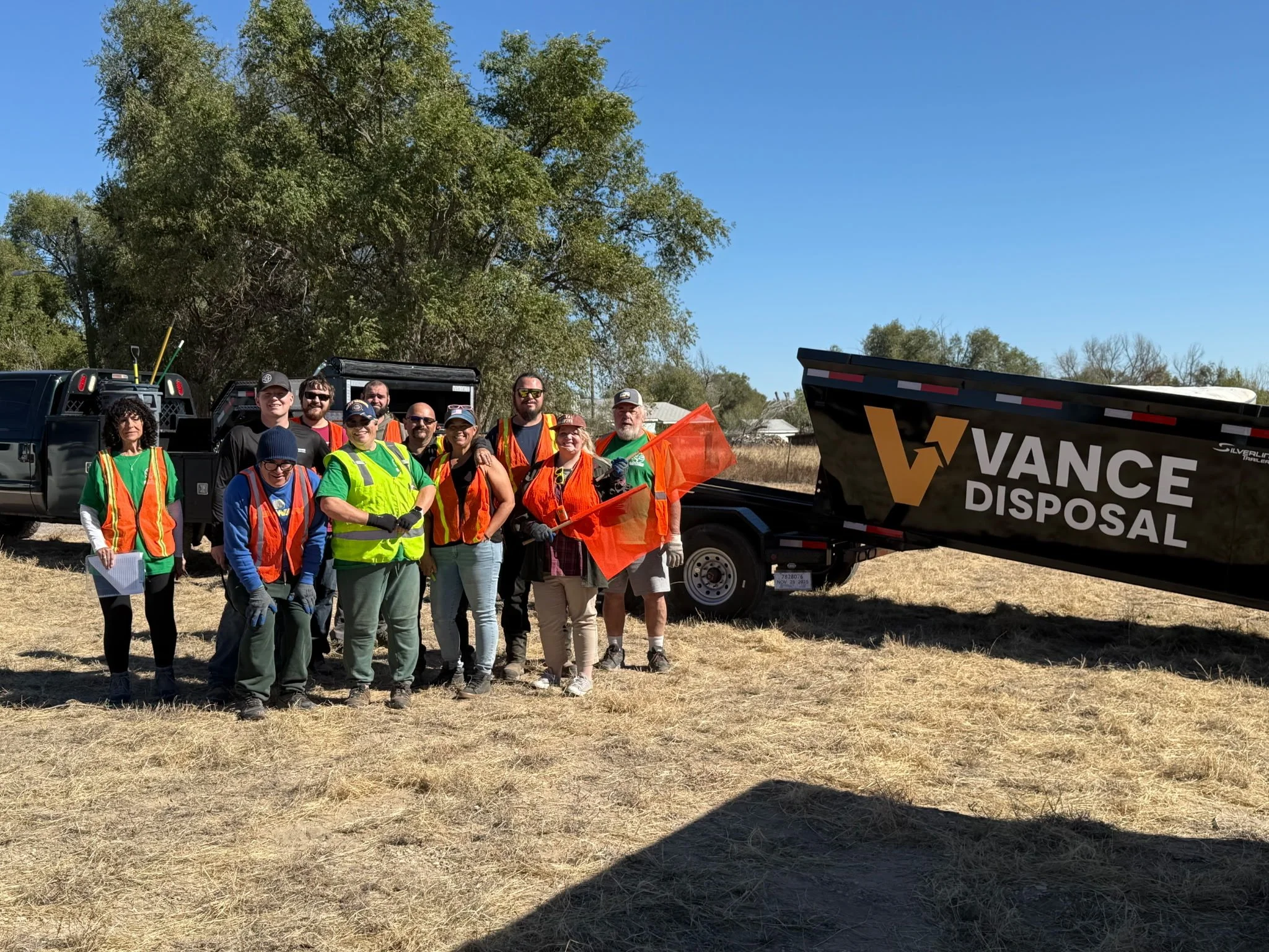 A large black dumpster filled with black plastic trash bags and some blue items, placed in an outdoor area near a brick building with a window.