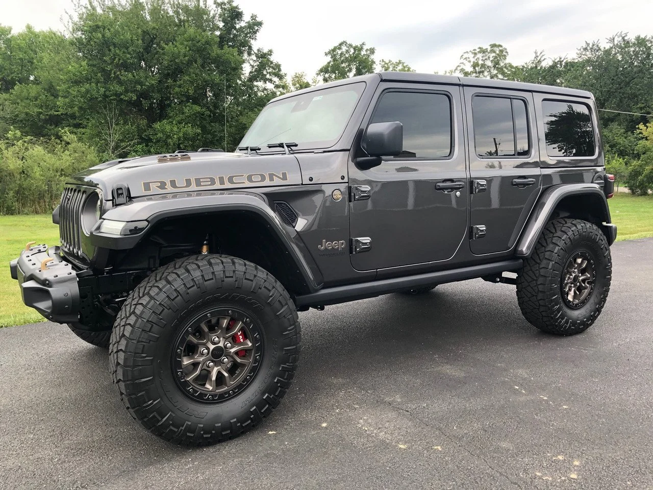 A black Jeep Wrangler Rubicon parked on a driveway with green trees in the background.