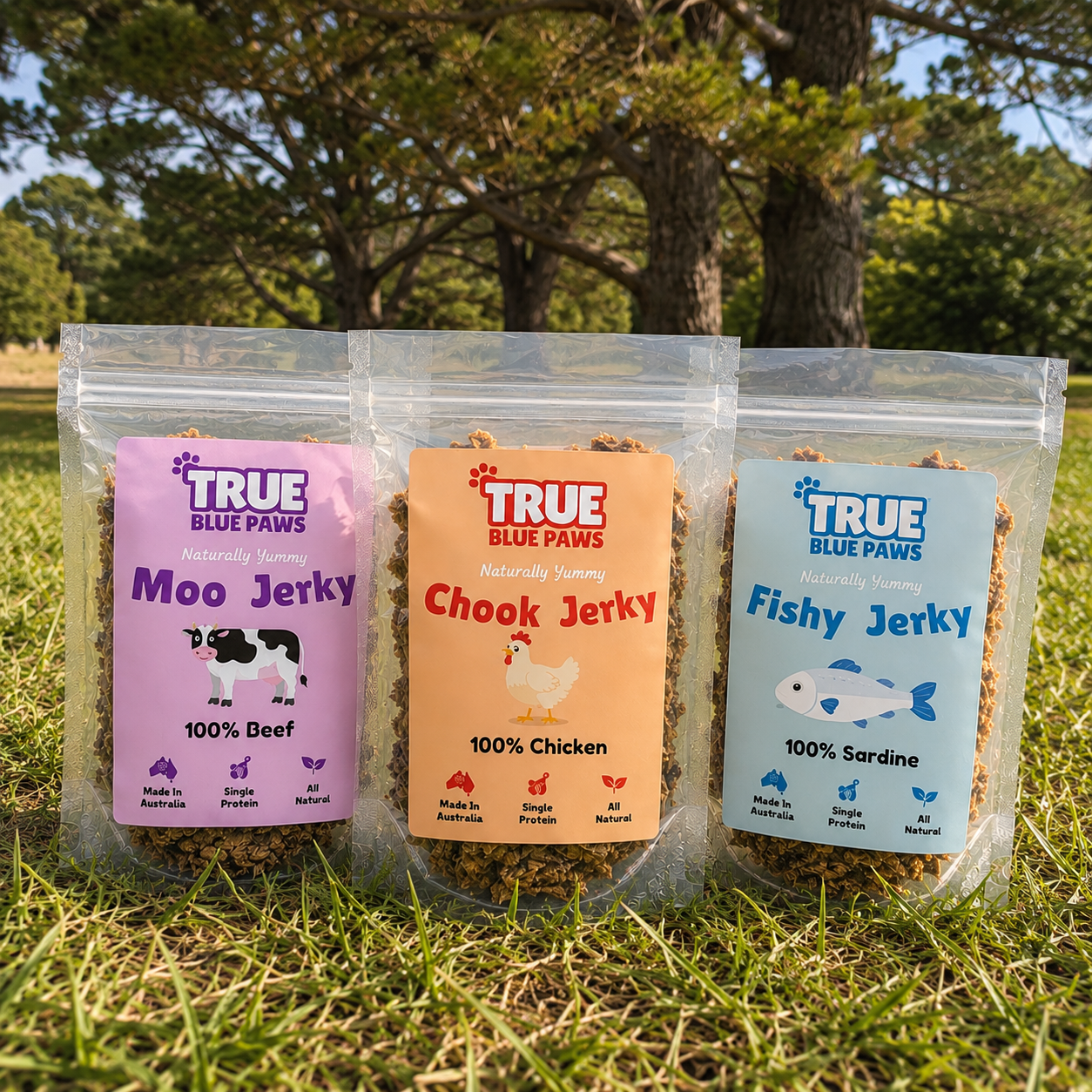 Three packages of dog jerky on grass with trees in the background. The packages are labeled Moo Jerky, Chook Jerky, and Fishy Jerky, made in Australia with natural ingredients and single protein sources, for dogs.