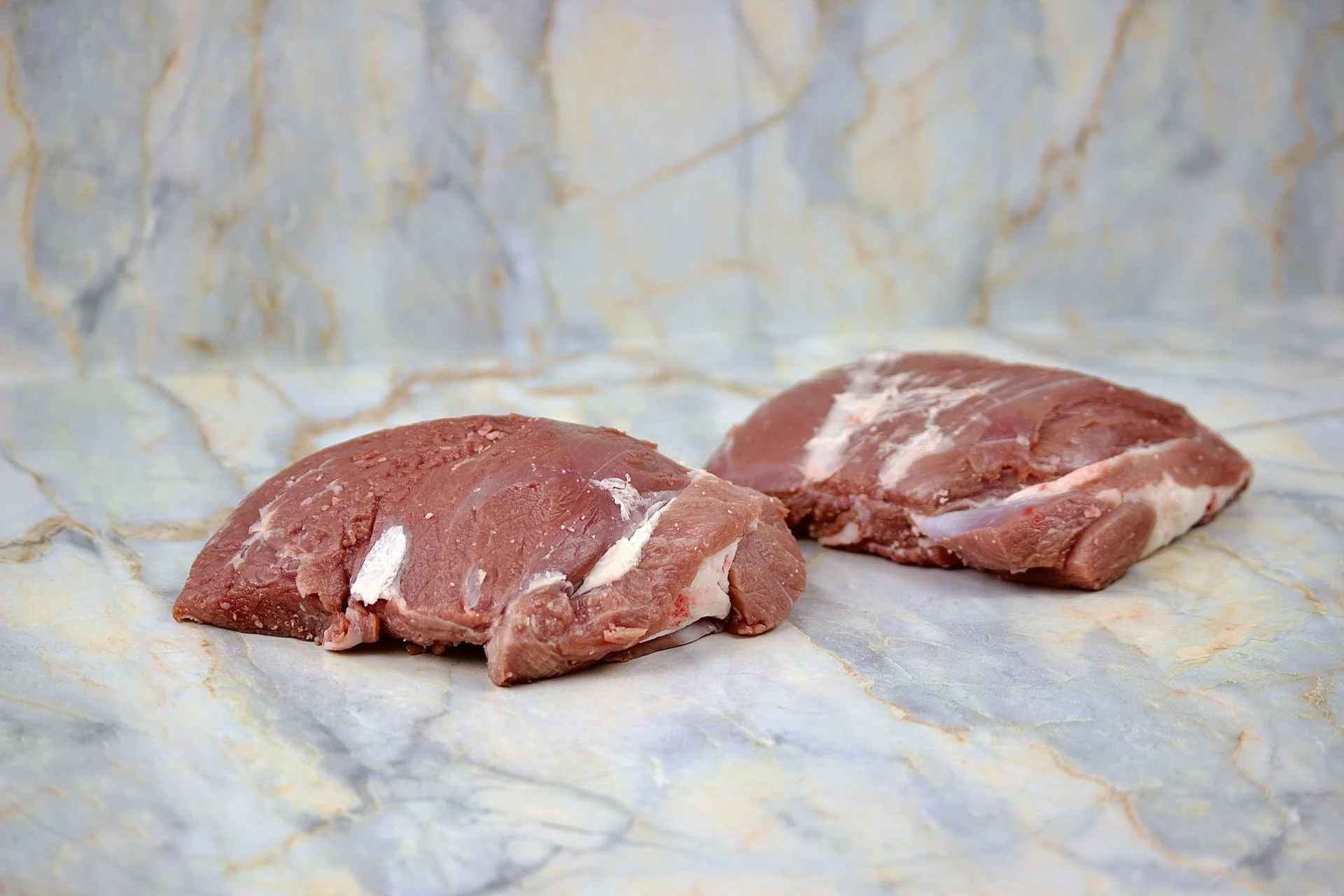 Two raw pork steaks on marble surface.