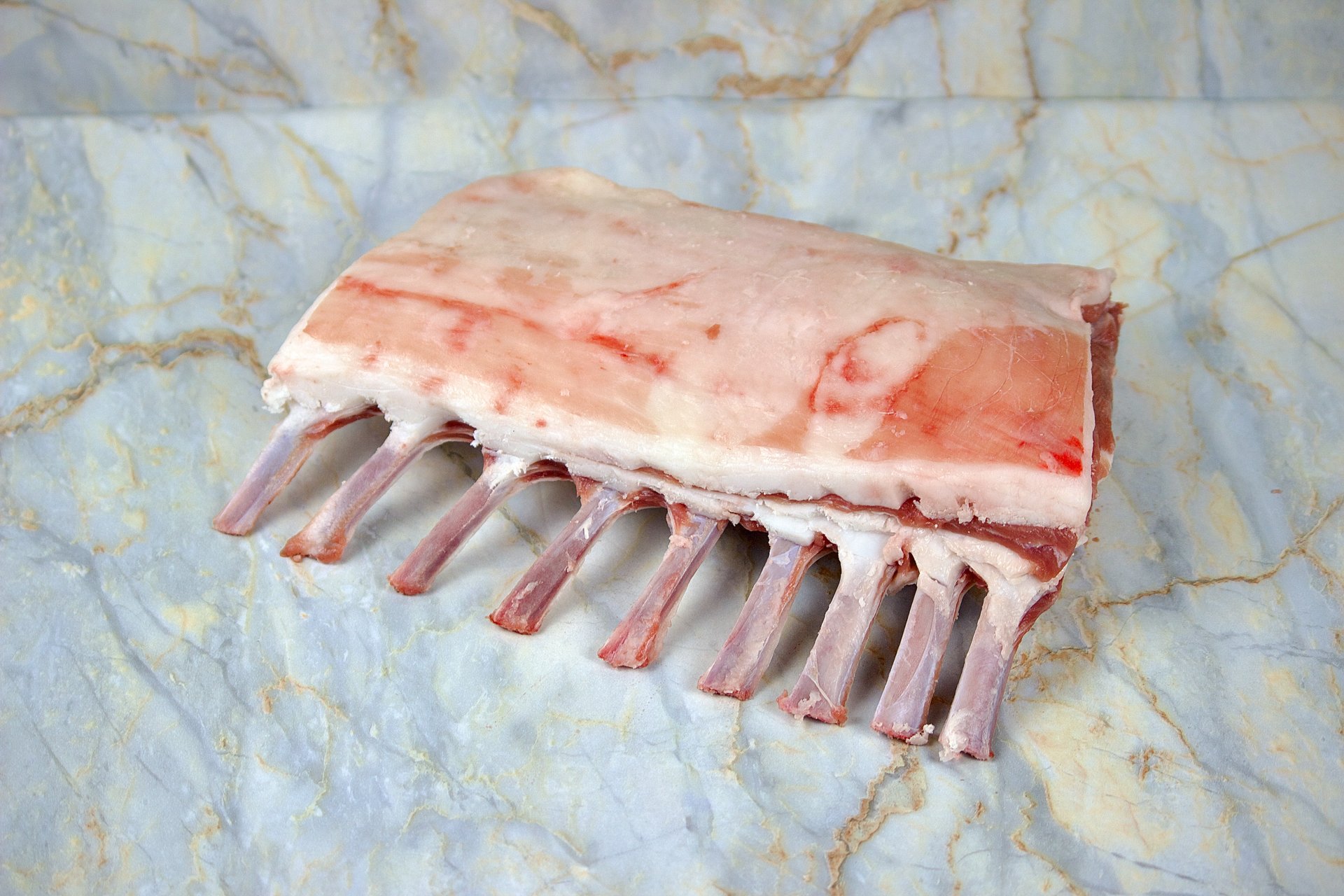 A raw beef short rib cut with bones, placed on a marble surface.