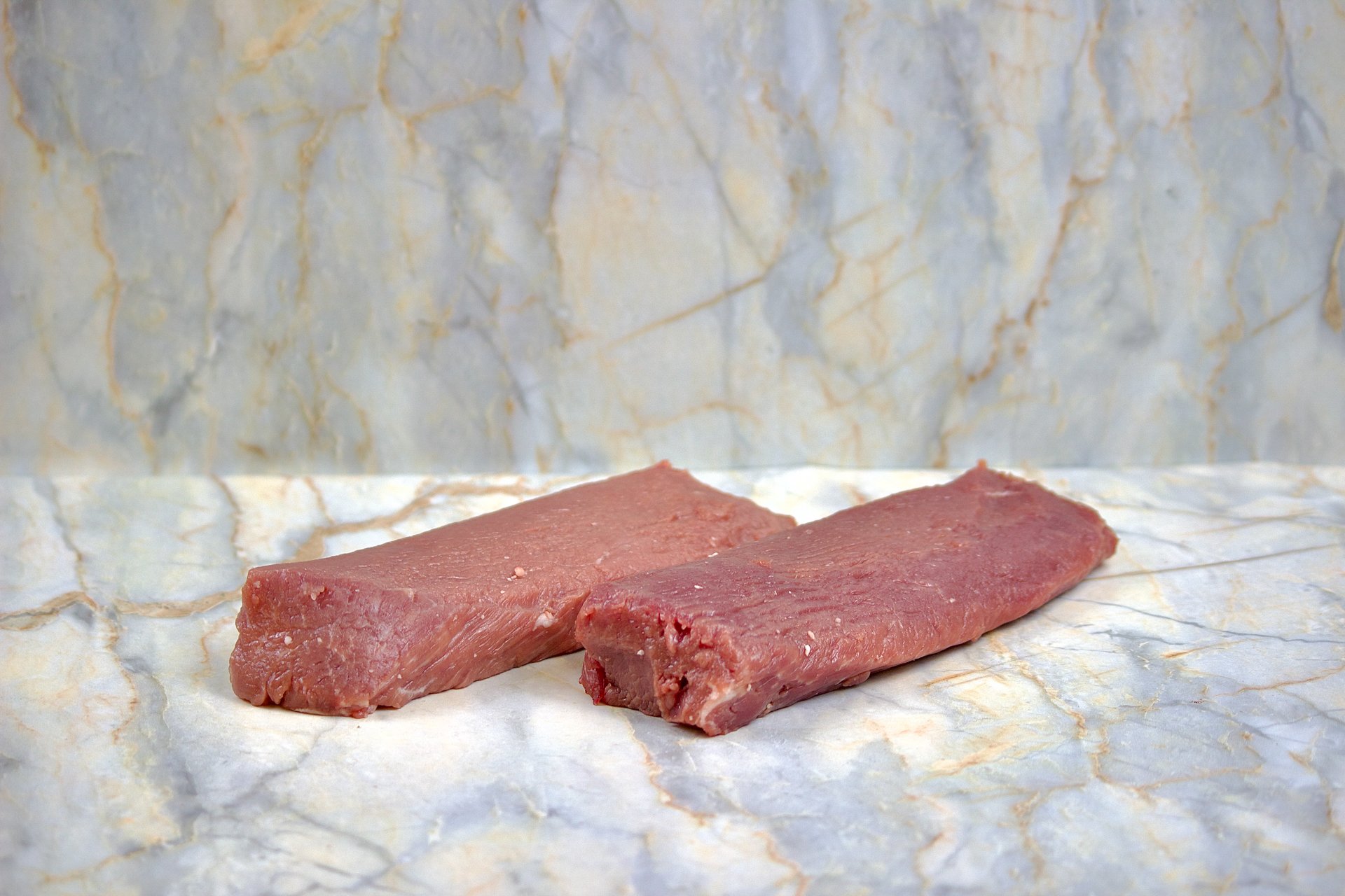Two raw pieces of beef steak on a marble surface with a marble background.
