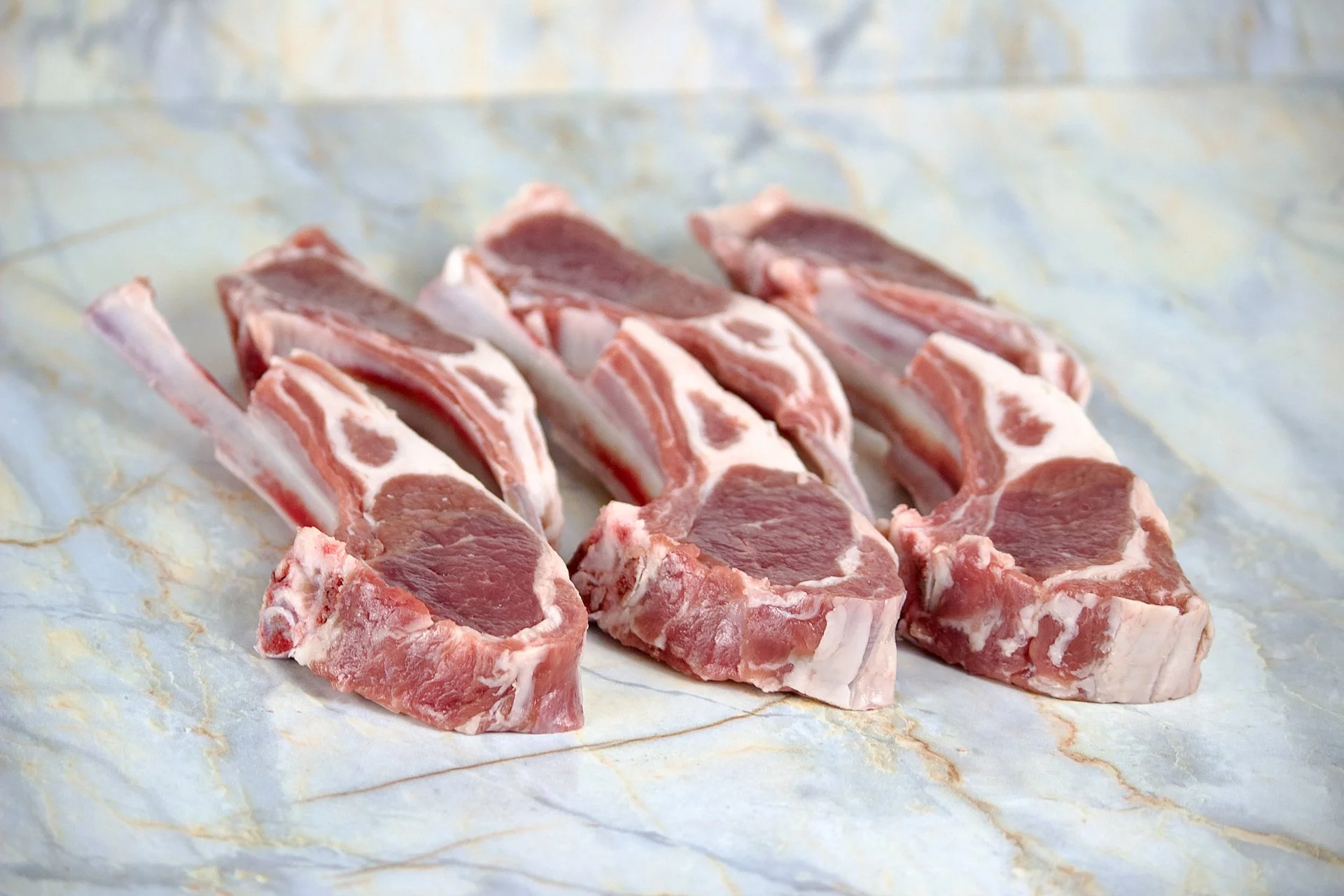 Raw pork chops with bone on a marble surface.