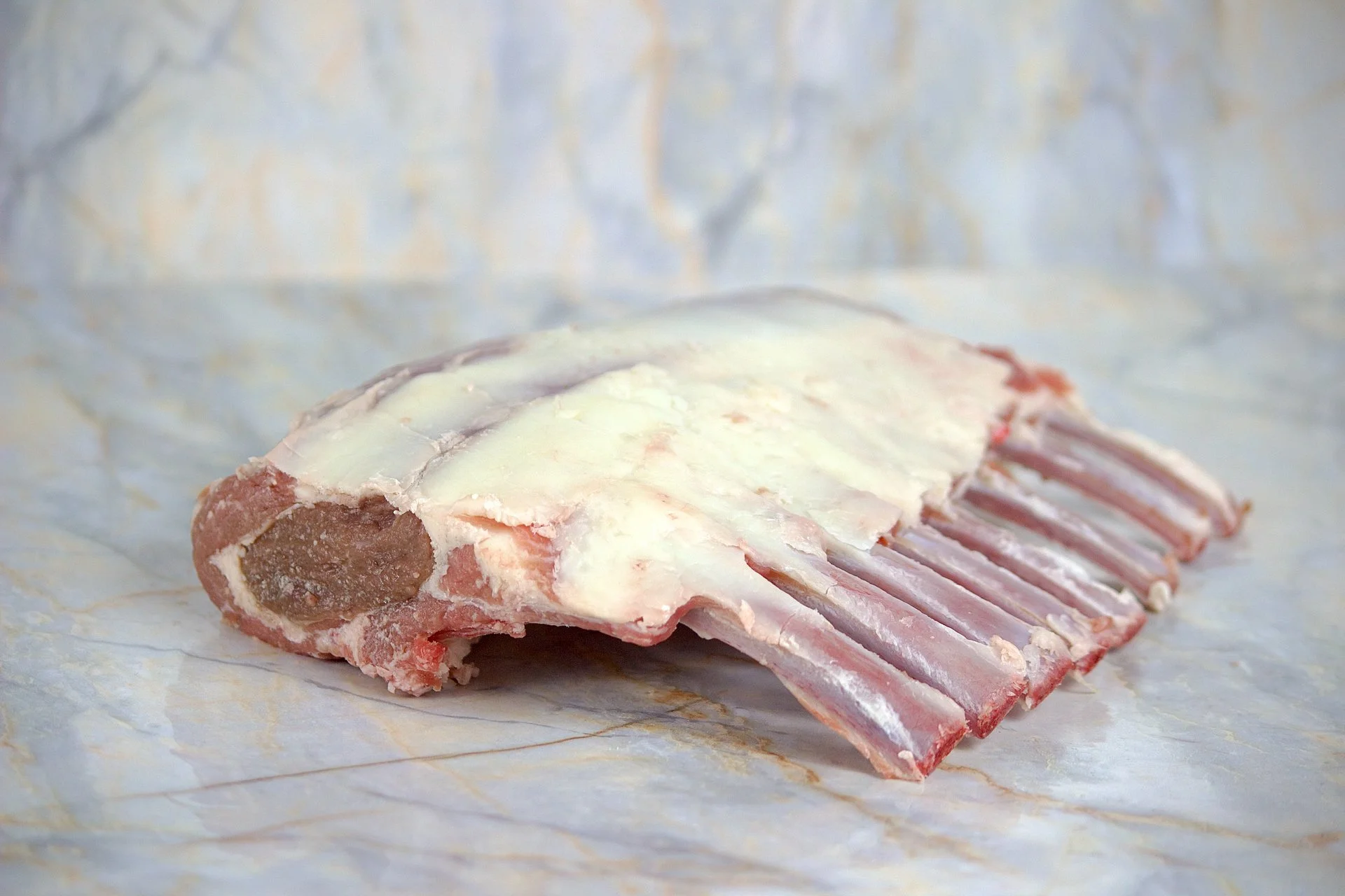 Raw rack of lamb with a layer of fat on top, resting on parchment paper.