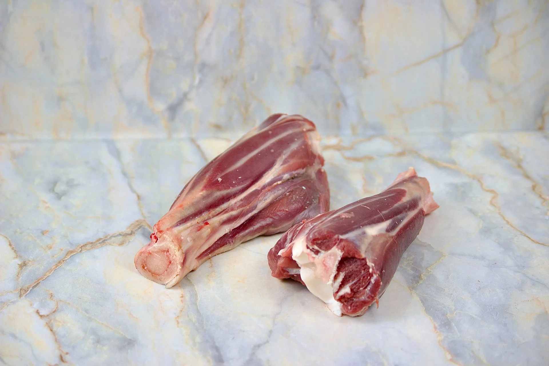 Two raw cuts of lamb shank on a marble surface.