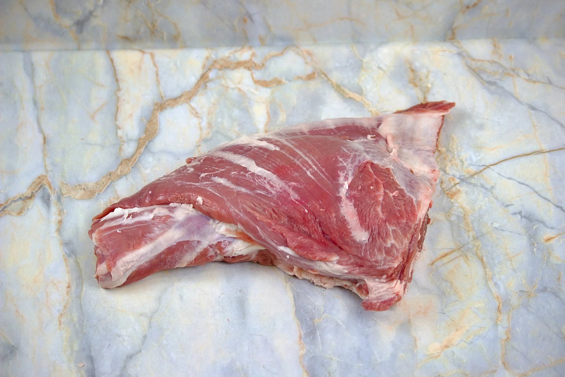 Raw piece of meat placed on a marble surface.