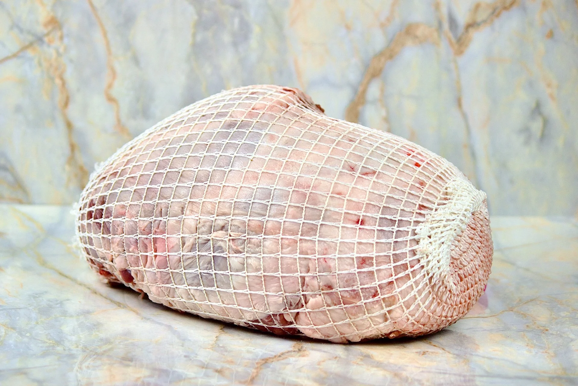Raw whole chicken in a netted bag on a marble surface with a marble background.
