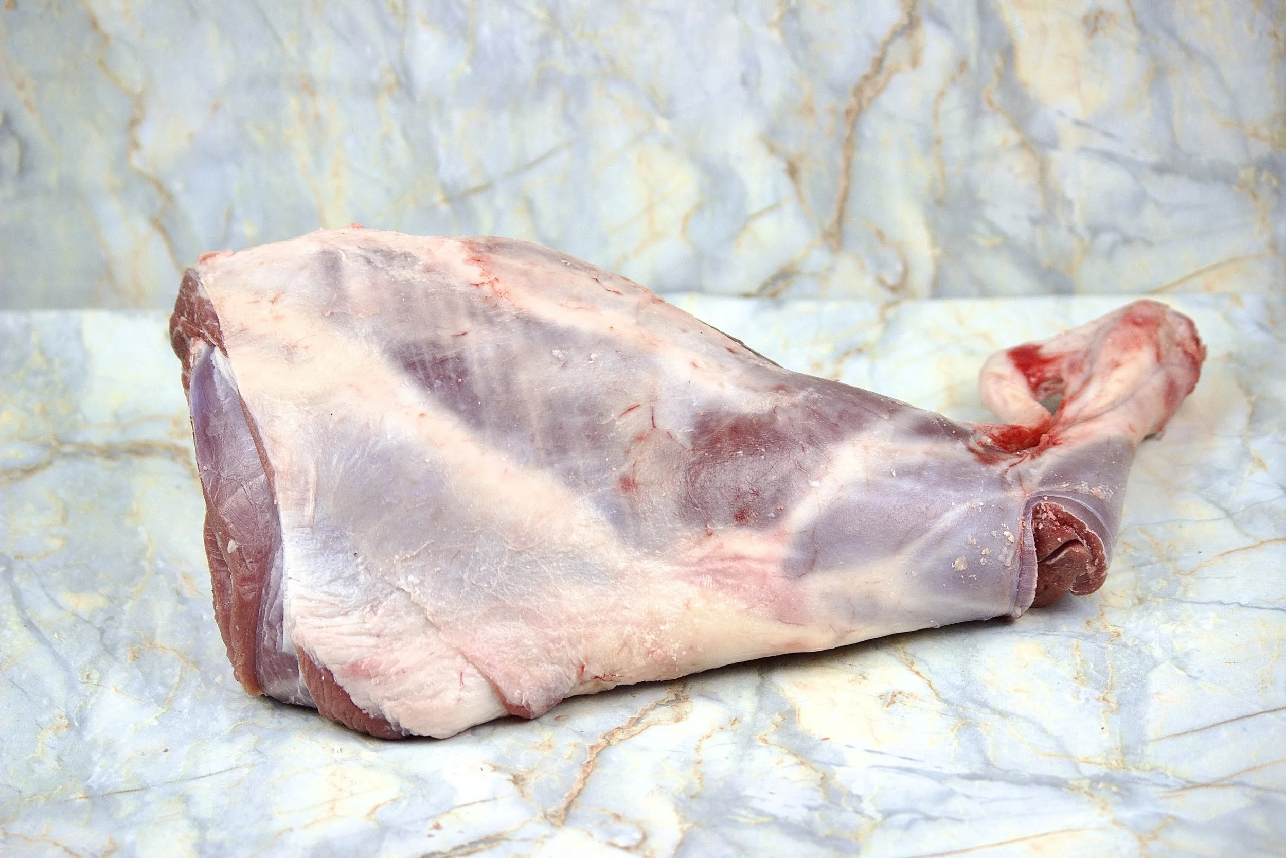 A raw, untrimmed lamb shank placed on marble paper.
