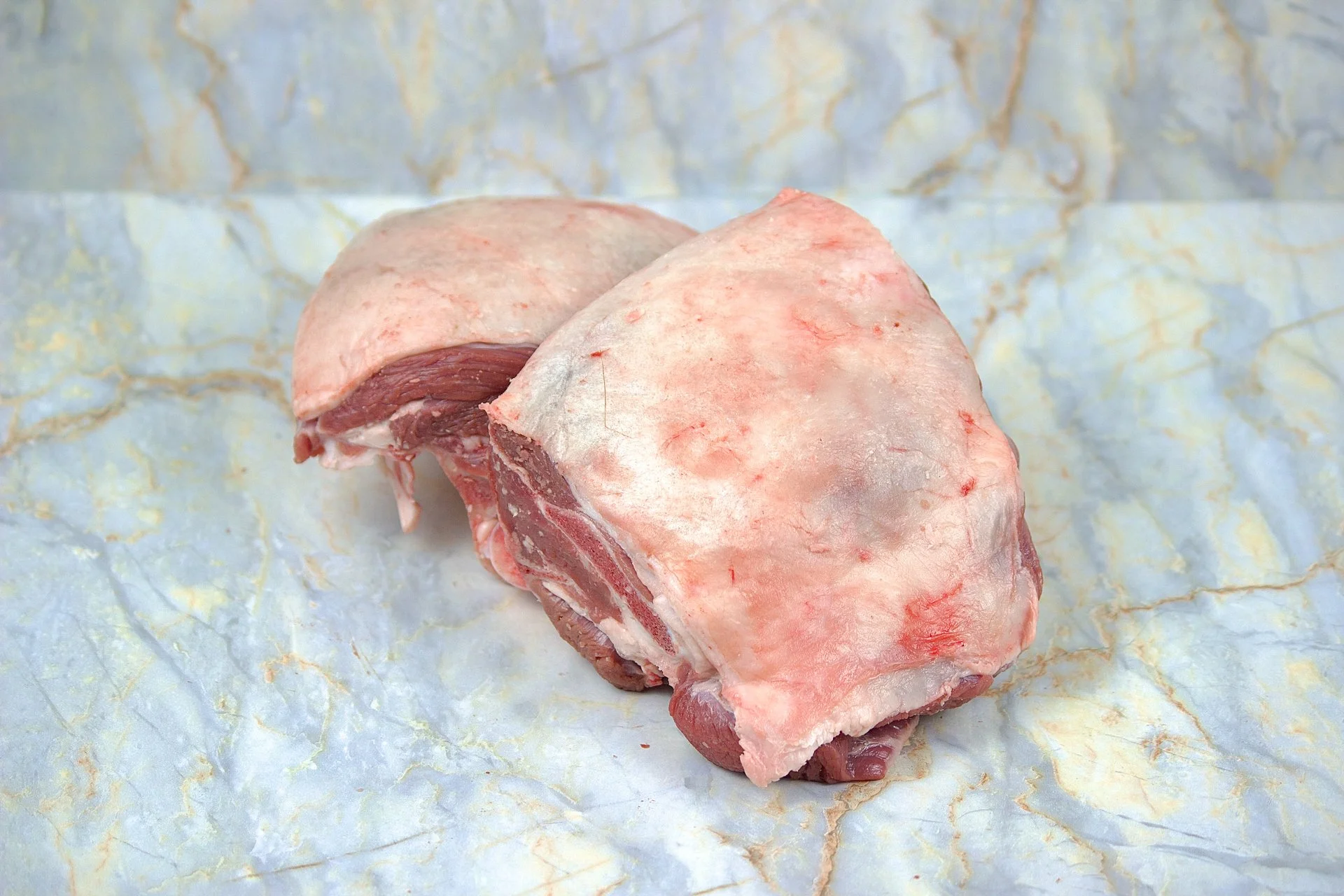 A cut of raw meat with bone on a marble surface.