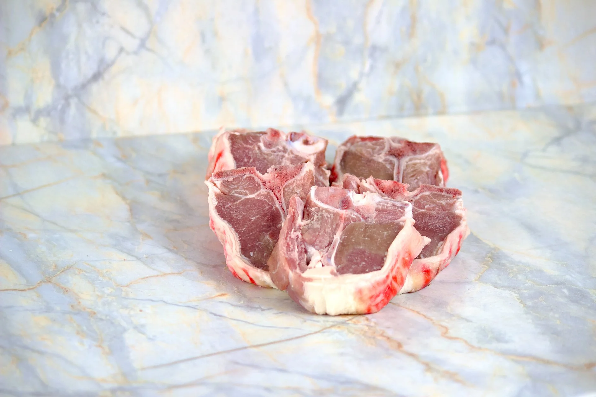 Raw pork chops with bone on a light-colored marble surface.