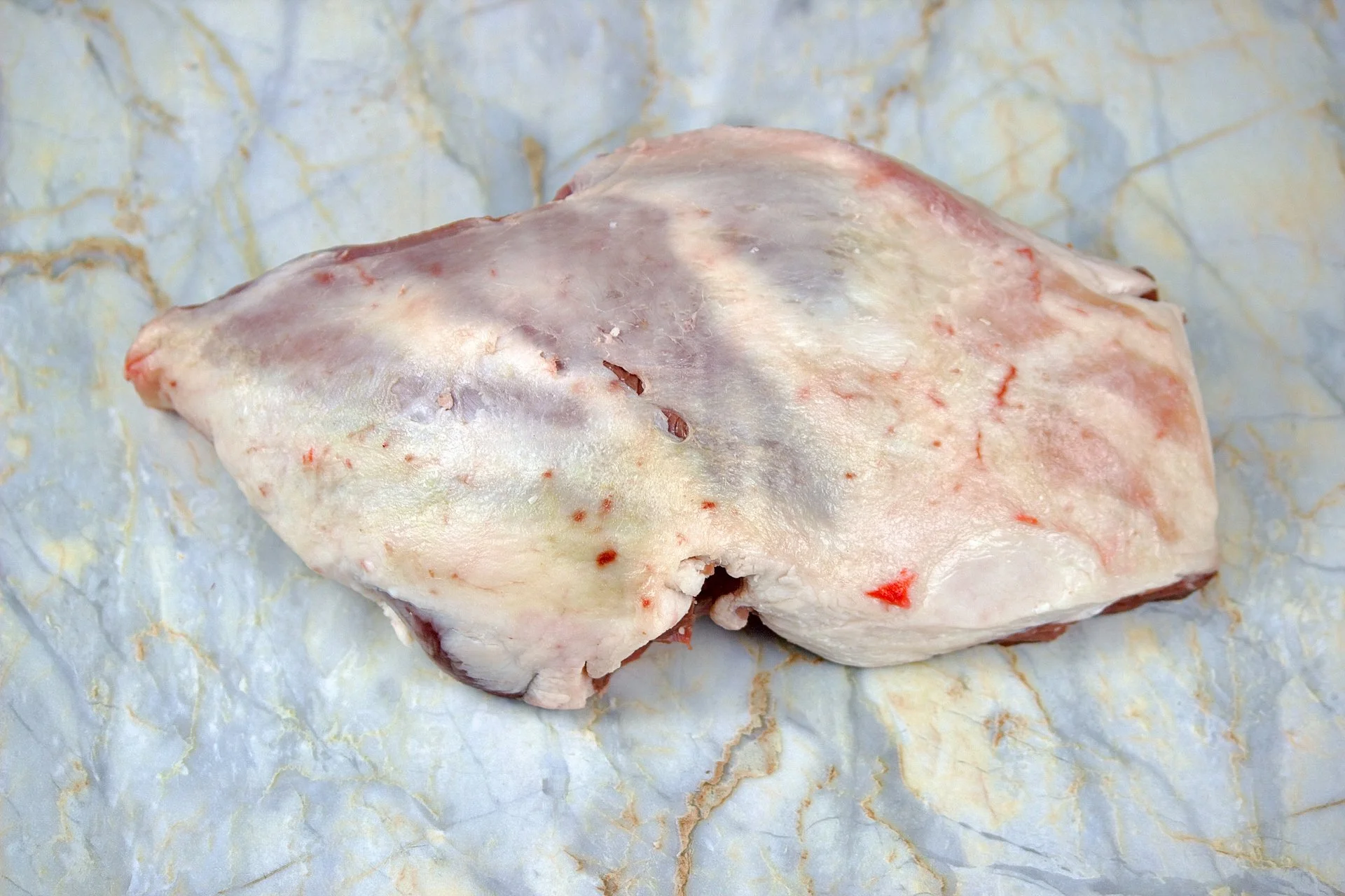Raw lamb shoulder covered with a thin layer of fat placed on marble surface.