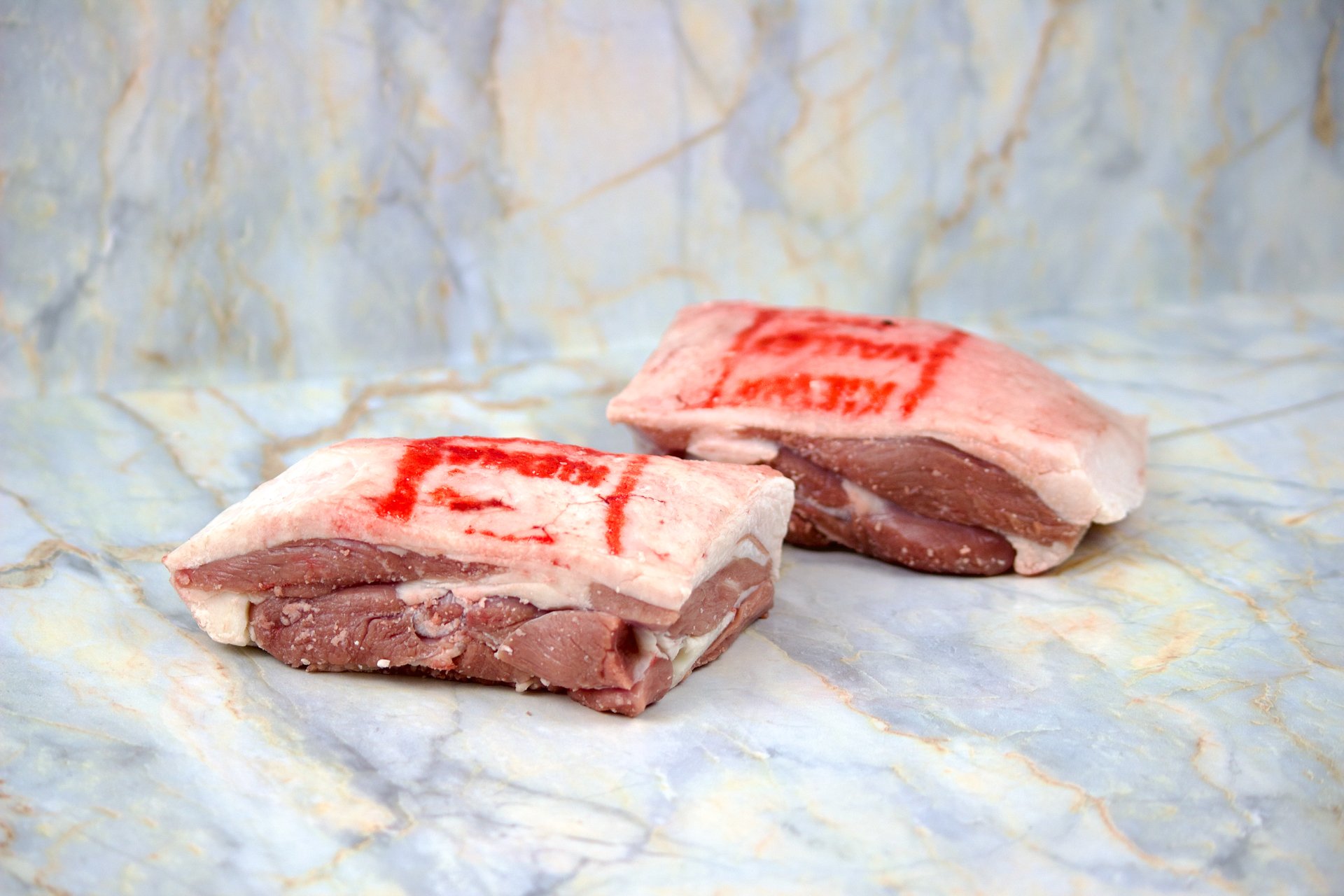 Two pieces of raw meat with red 'MEAT' stamp on a marble surface.