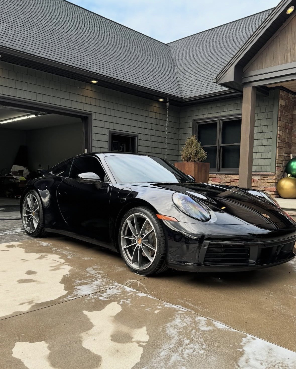 A black Porsche sports car parked outside a house on a wet driveway.