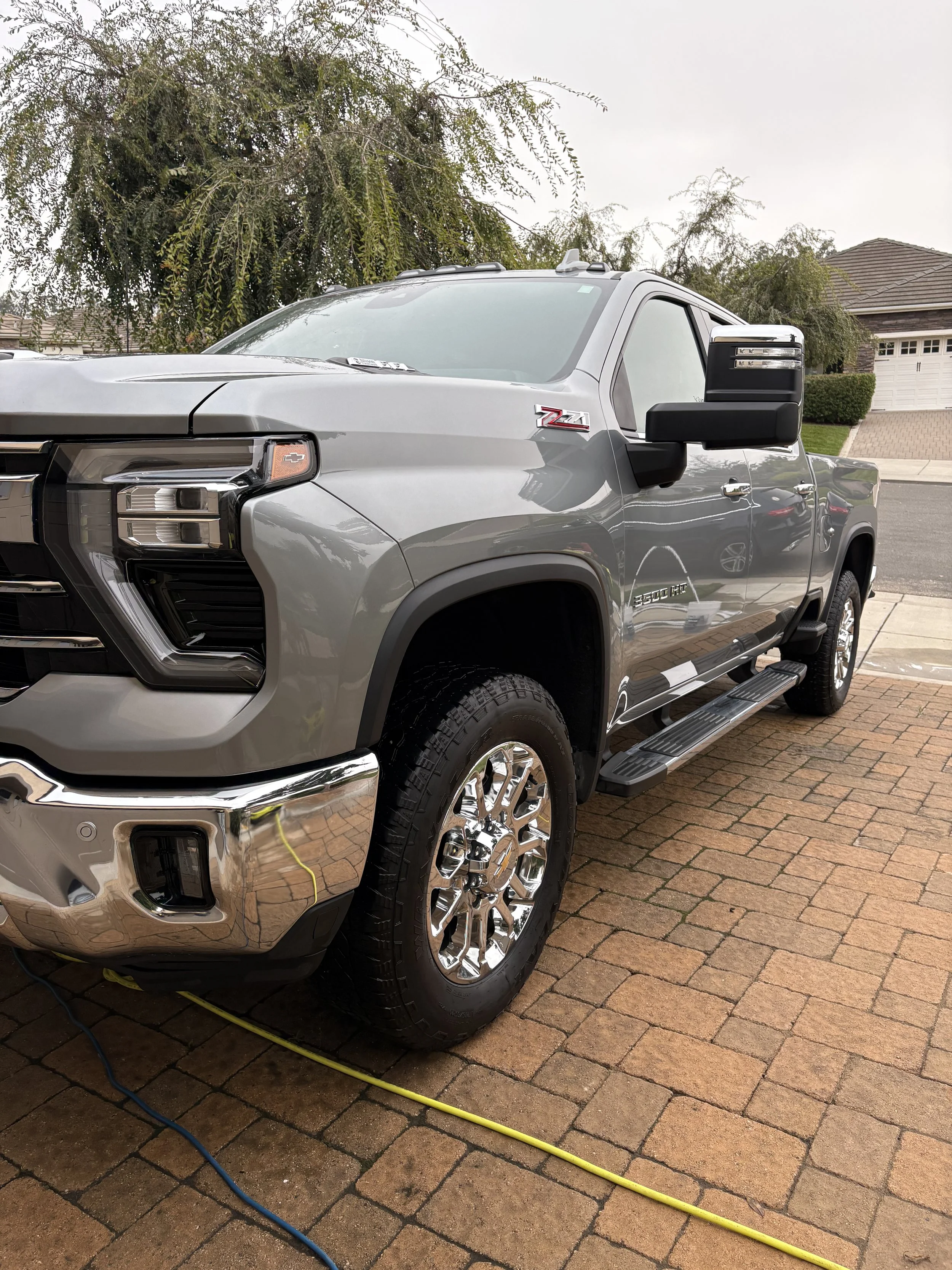 Silver GMC Sierra HD parked on a brick driveway in Nipomo, CA, freshly detailed by Fastlane Detailing with trees in the background