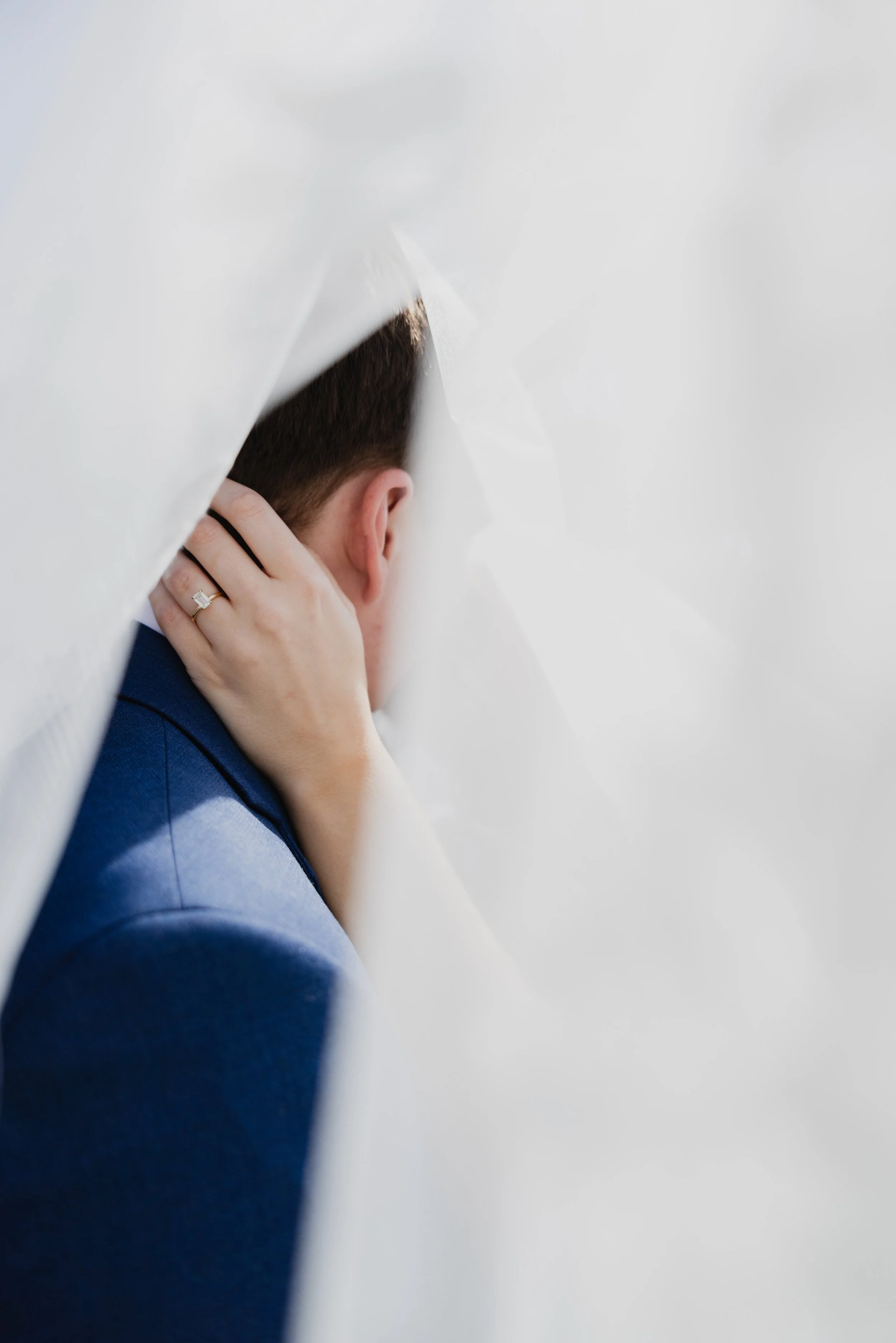 Side profile of a man in a blue suit with his hand gently touching his neck, viewed through a white, semi-transparent material.