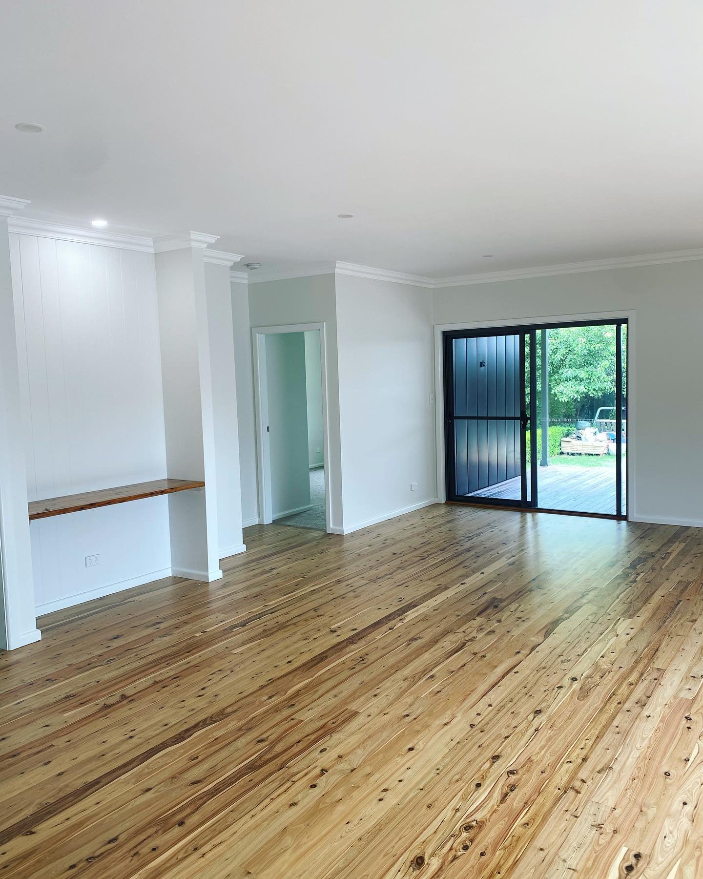 Empty living room with hardwood floors, white walls, a sliding glass door leading outside, and a small built-in wooden shelf.