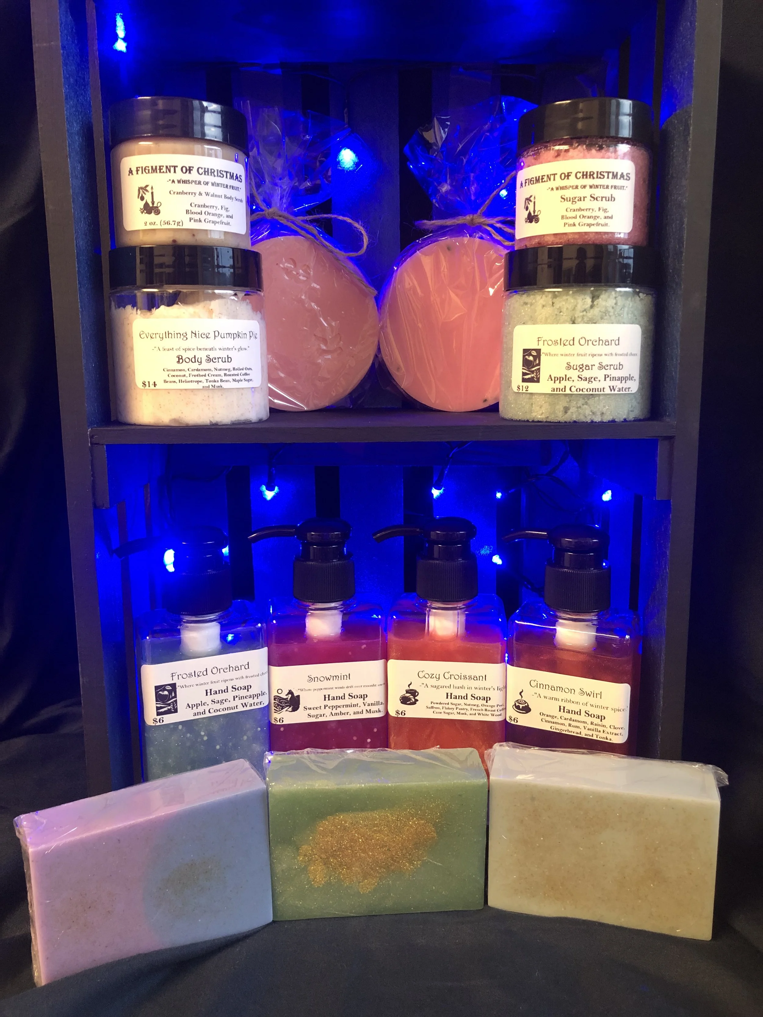 Shelf with scented candles and soap bars, decorated with Christmas-themed labels and blue string lights.