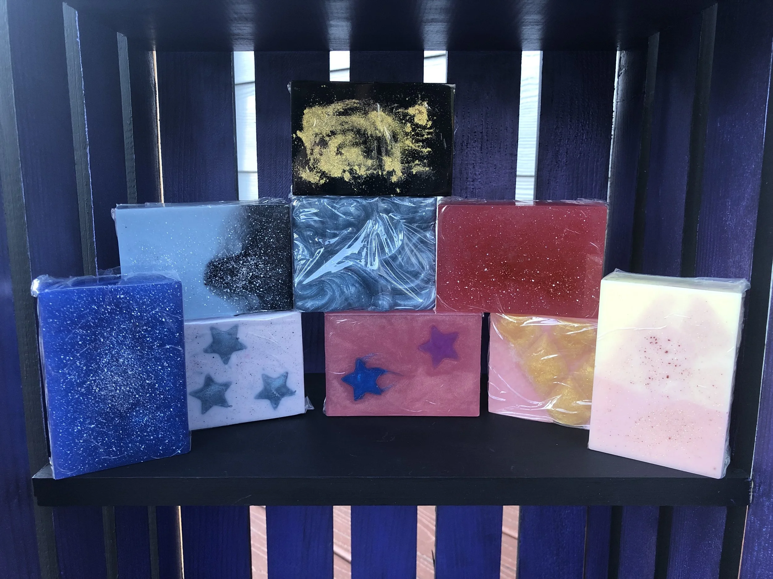 Colorful artisan soaps with star-shaped decorations on display on a black shelf with dark blue background.