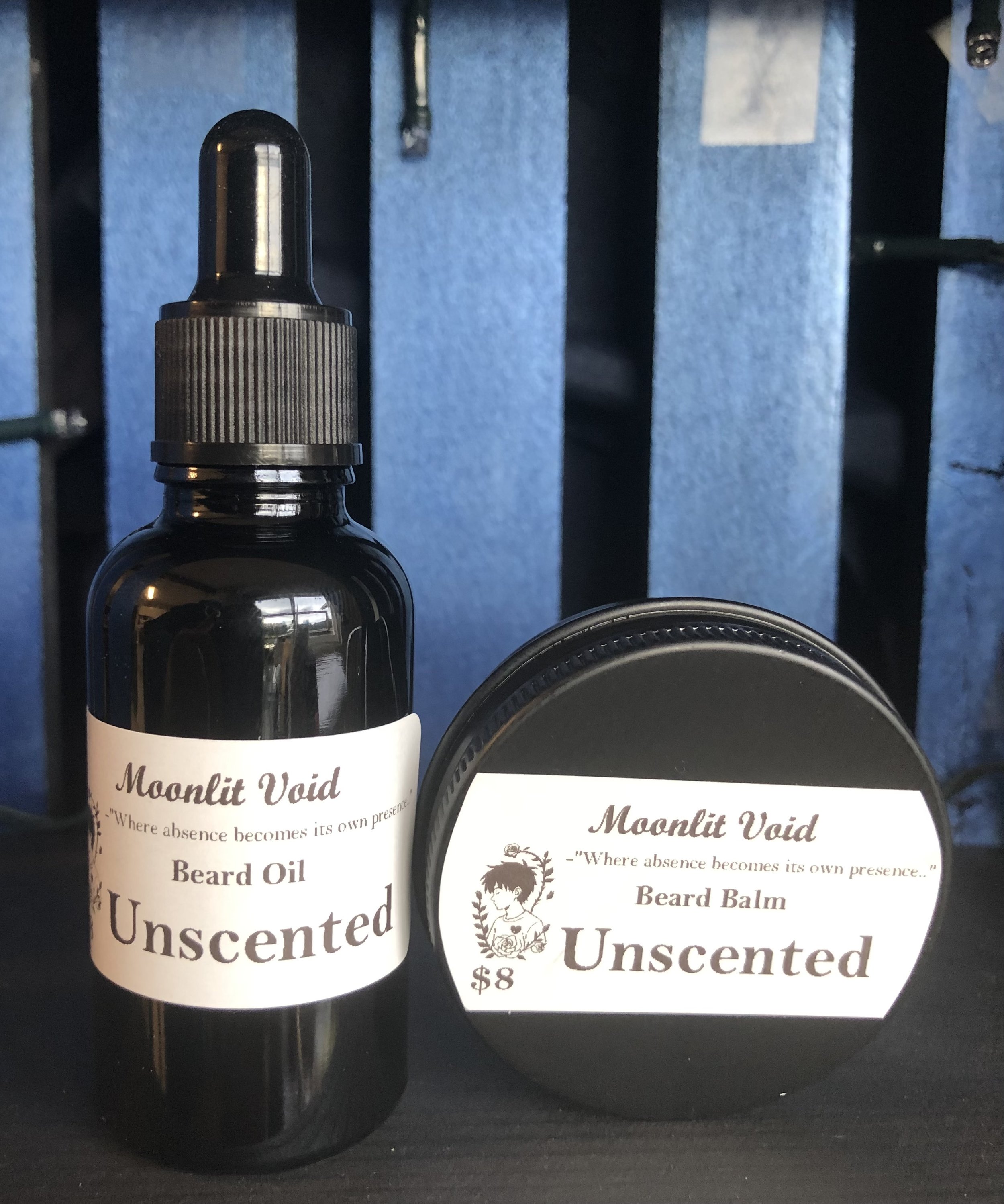 Two black containers of beard care products labeled Moonlit Void, including a beard oil and a beard balm, both inscribed as unscented.