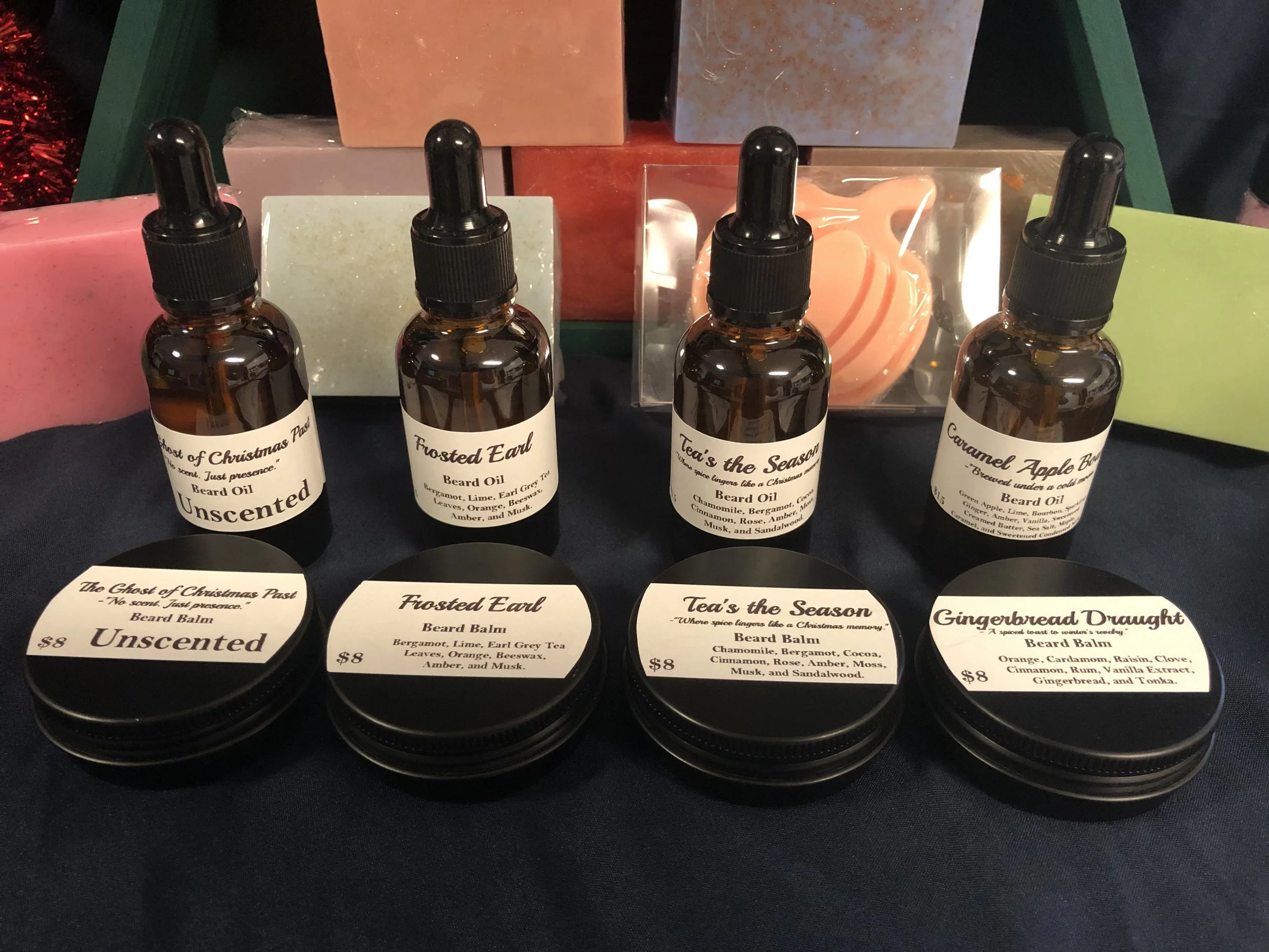 Collection of beard oils and beard balms with holiday-themed labels and packaging on a dark surface.