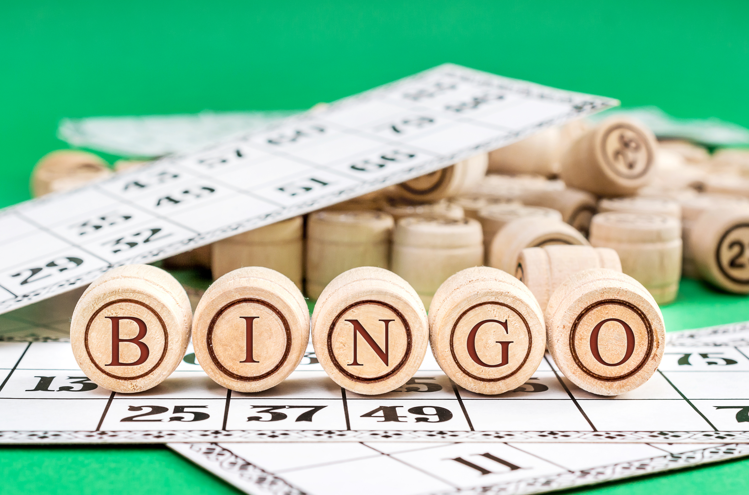 Wooden bingo number tiles spelling out BINGO with bingo cards and wooden bingo balls on a green background.