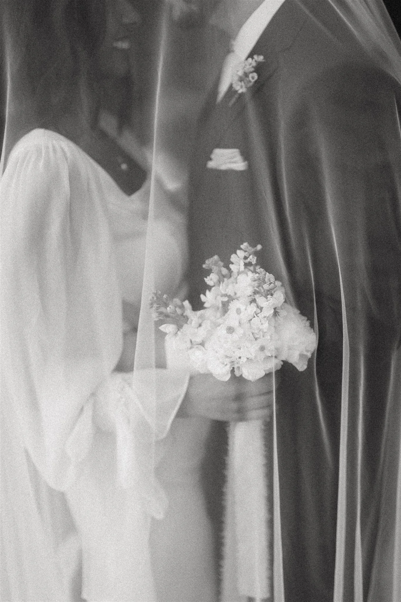 Black and white photo of a bride holding a bouquet of flowers, wearing a wedding dress and a veil.